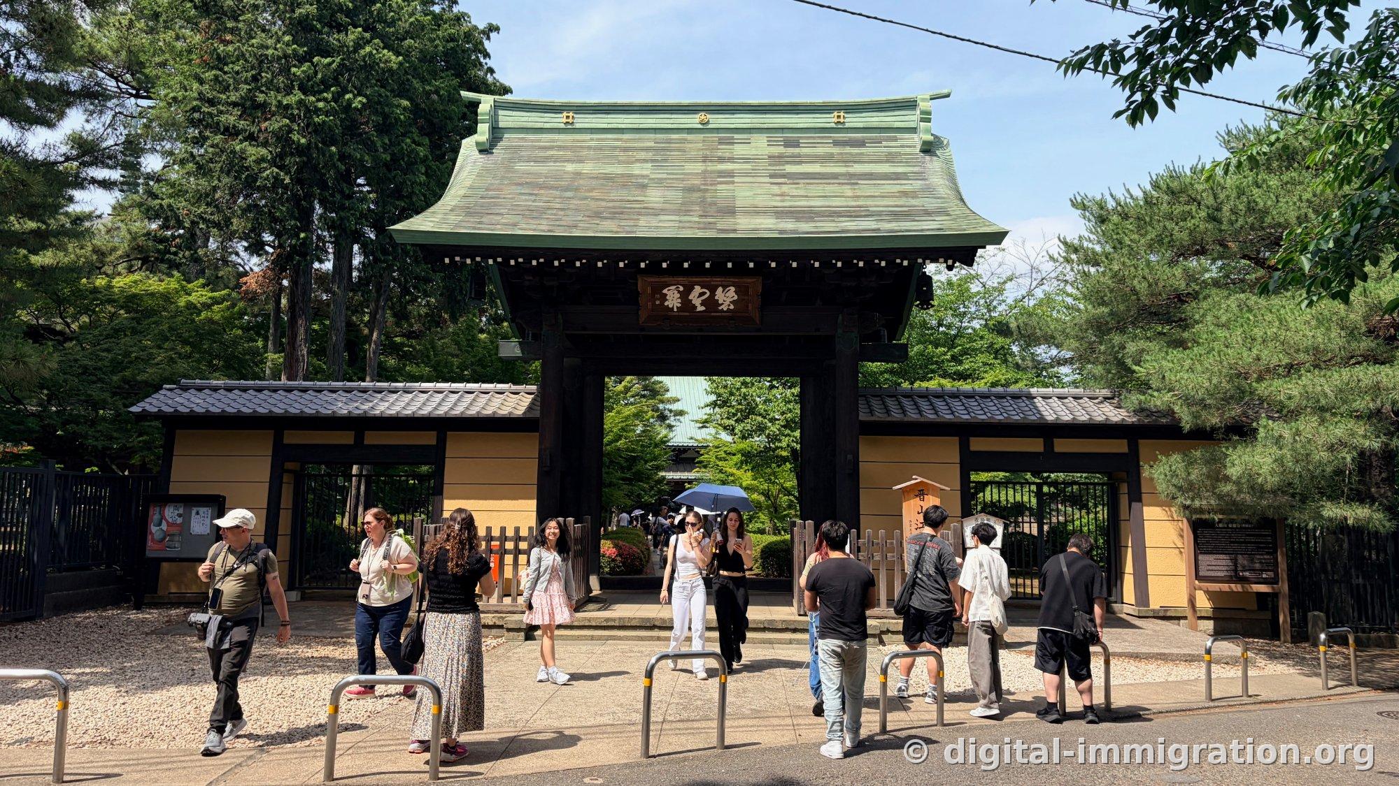 The sanmon gate of Gotokuji with a verdigris bronze roof and visitors of various nationalities passing through it