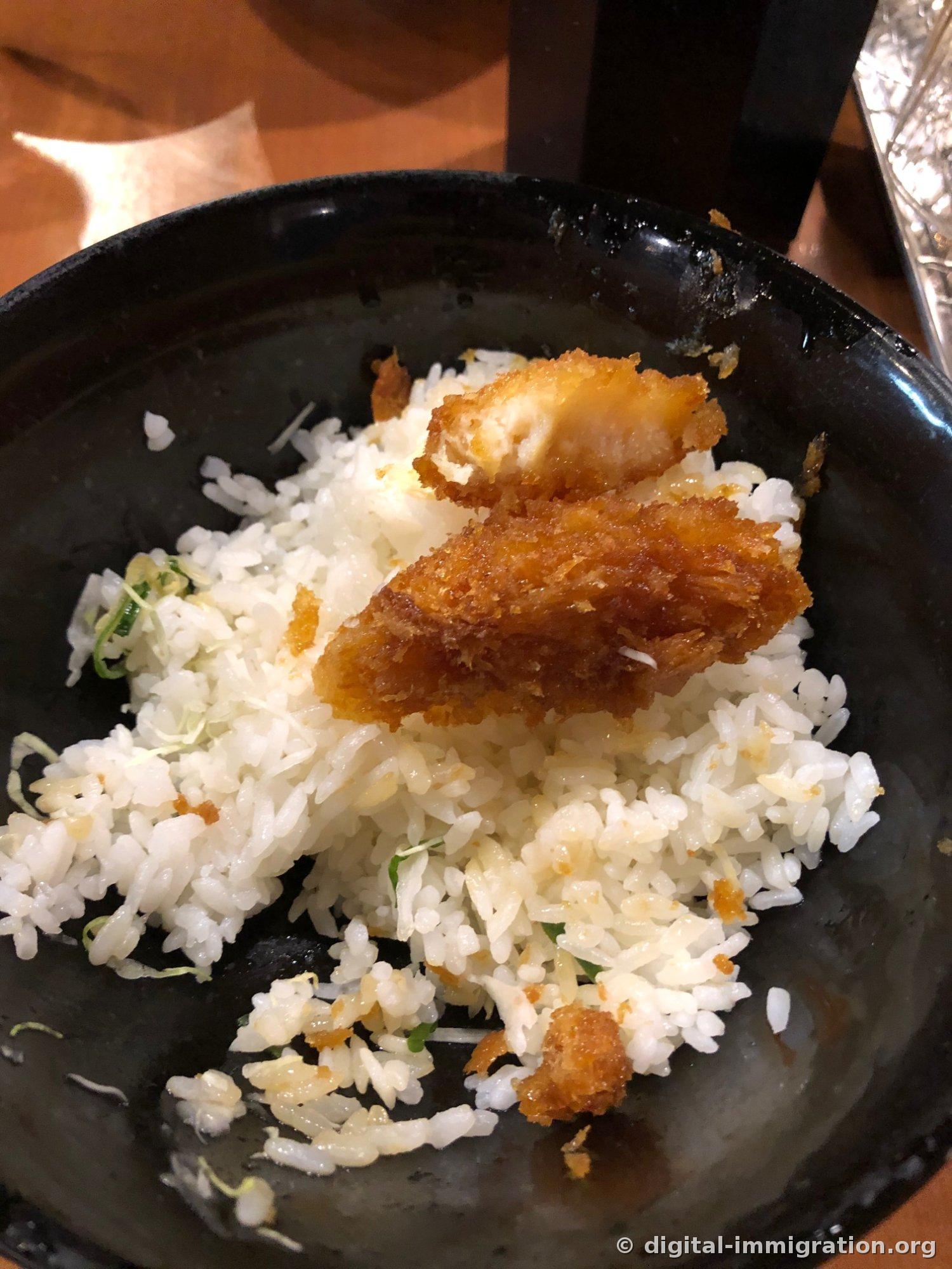 Un bol noir de riz garni presque fini, avec seulement du riz blanc et quelques morceaux de friture restants