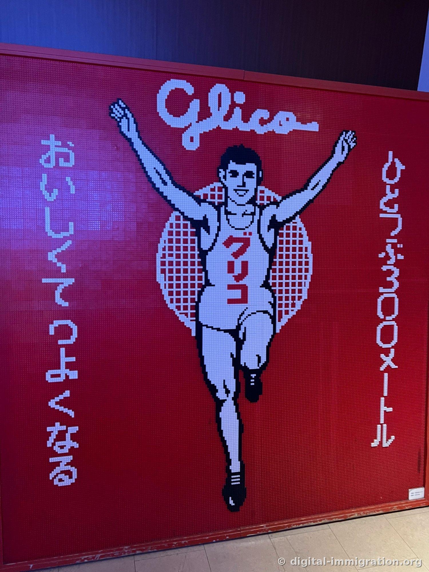 A Glico runner wall made of red pixels with the Japanese slogan 'One piece covers 300 meters'