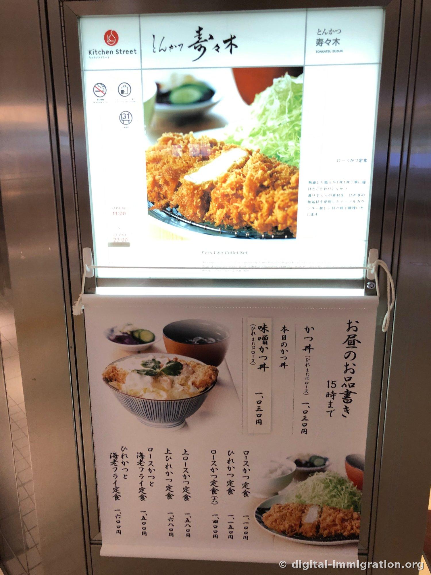 Kitchen Street标志和写有'とんかつ 寿々木 TONKATSU SUZUKI'的灯箱指示牌，下面贴着午餐菜单价格表