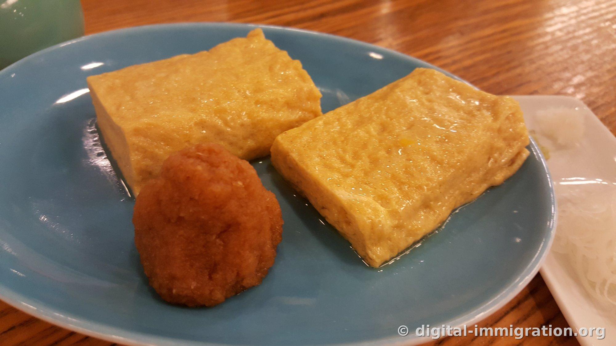 Deux épaisses tranches de tamagoyaki dashi dans une assiette bleue avec du momiji oroshi au piment, et du radis râpé blanc dans une assiette blanche à côté
