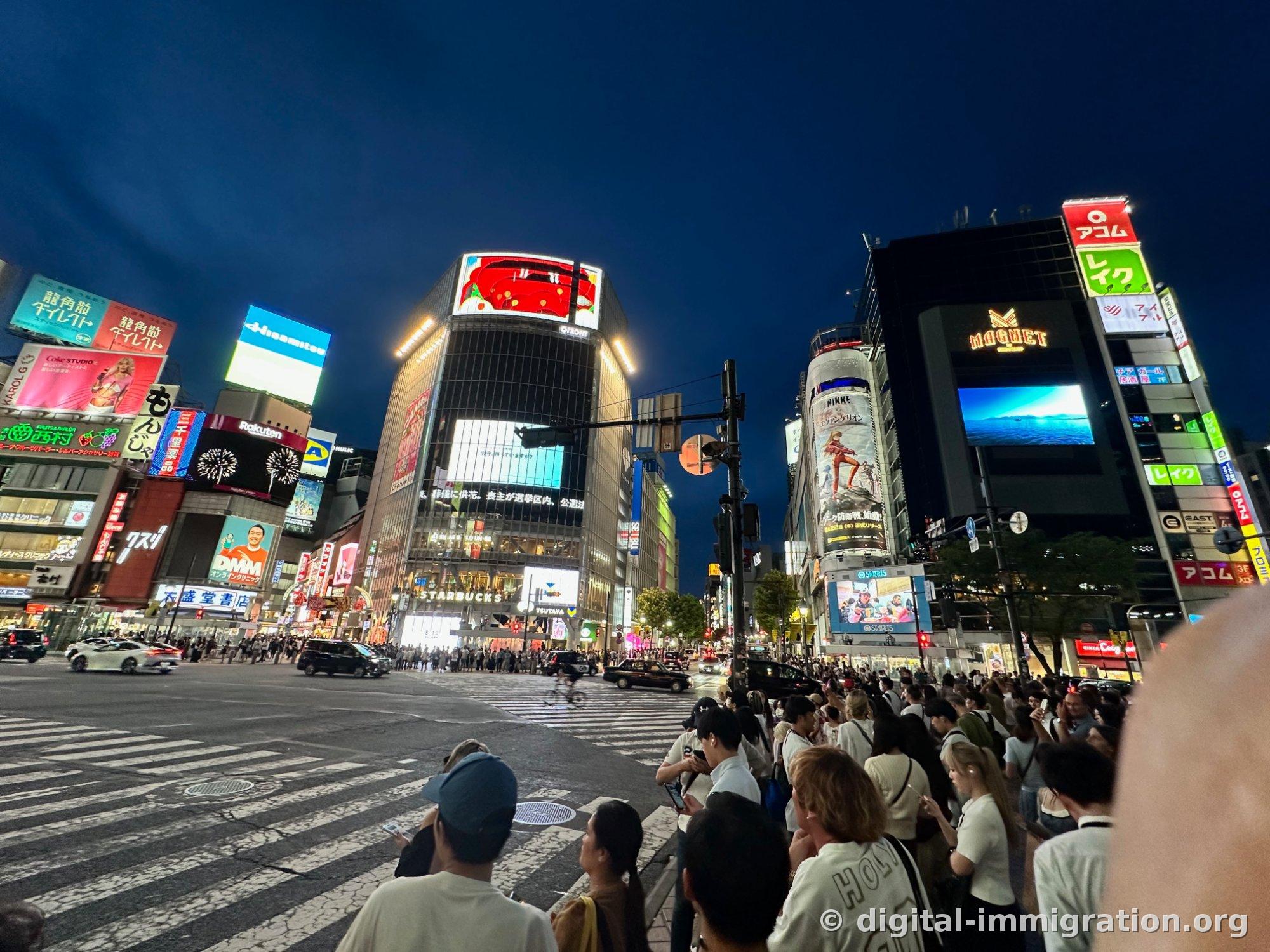 横断歩道の前で信号を待つ人たちの後ろにQFRONTとアコム、レイク のネオン看板が連なる夜景