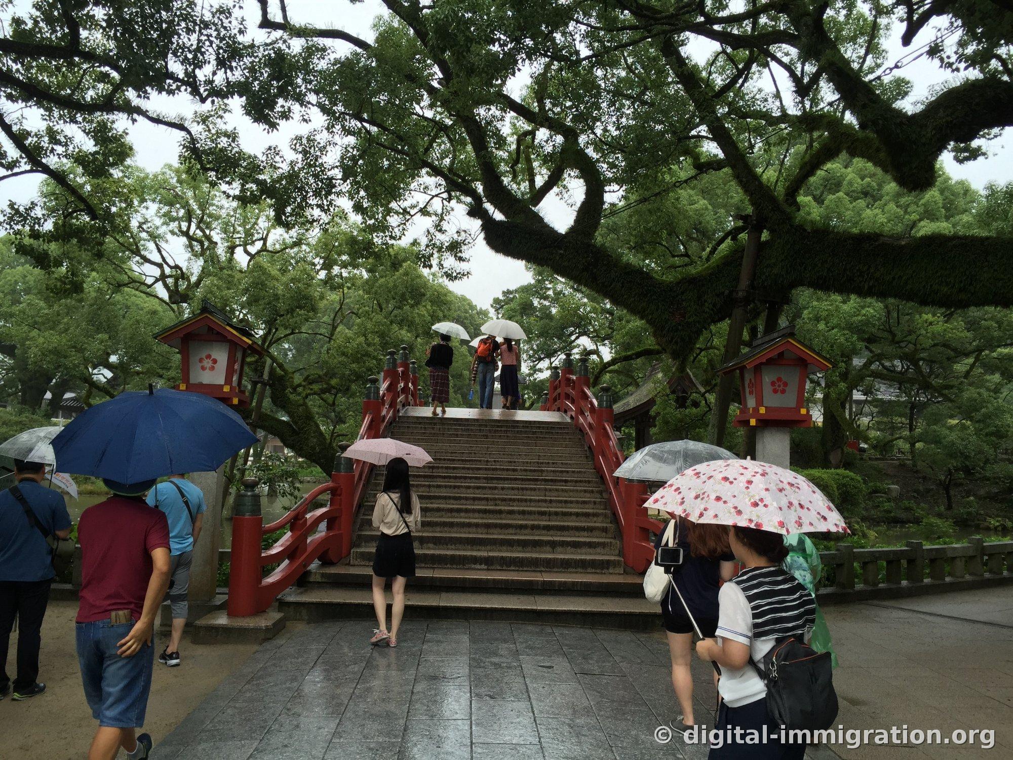Worshippers with umbrellas climbing the arched Daikoubashi steps with red railings, stone lanterns with plum blossom designs on both sides