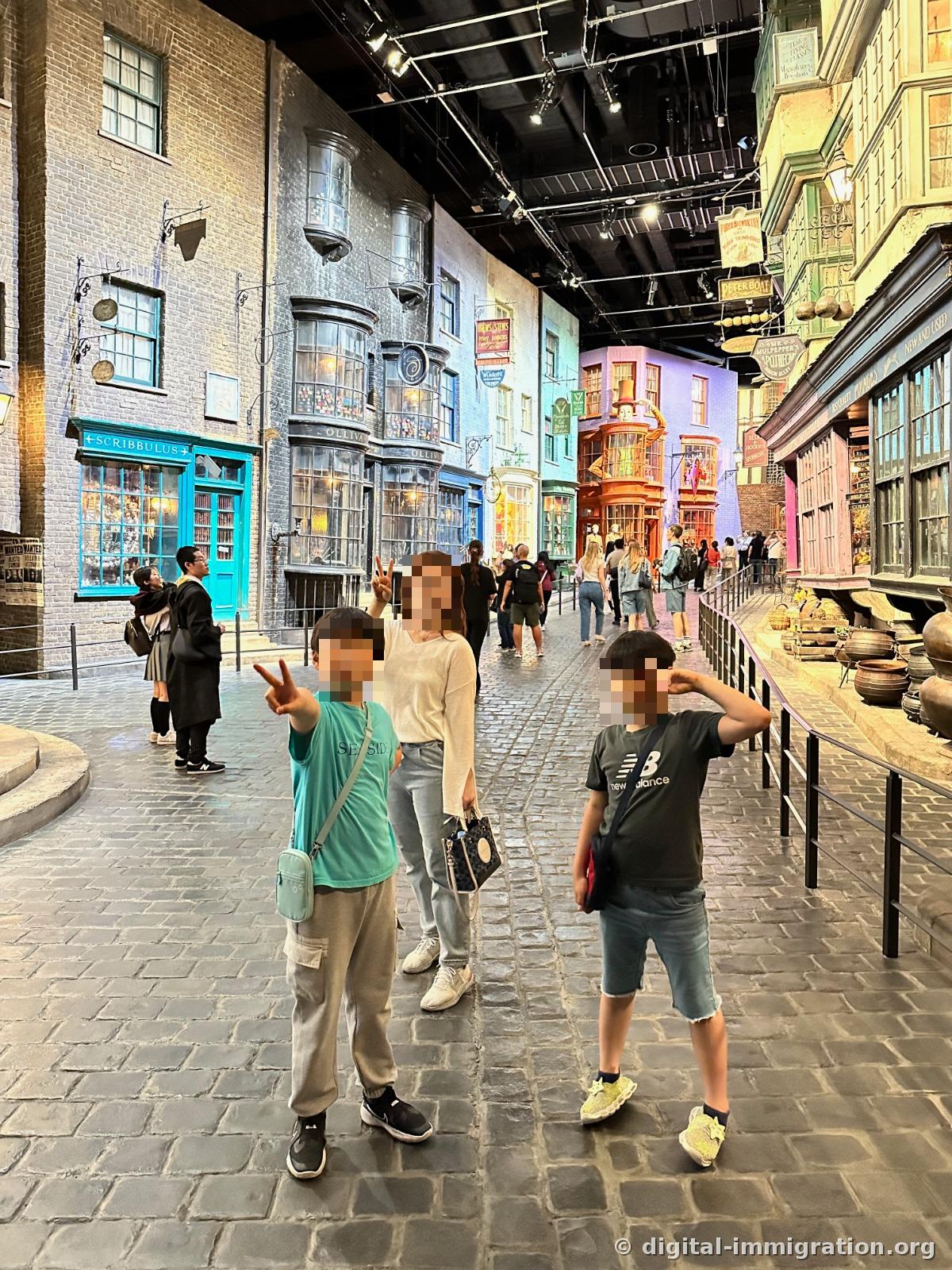Three people posing on a cobblestone street set with storefronts, including signs for Scrivenshaft's and Ollivander's
