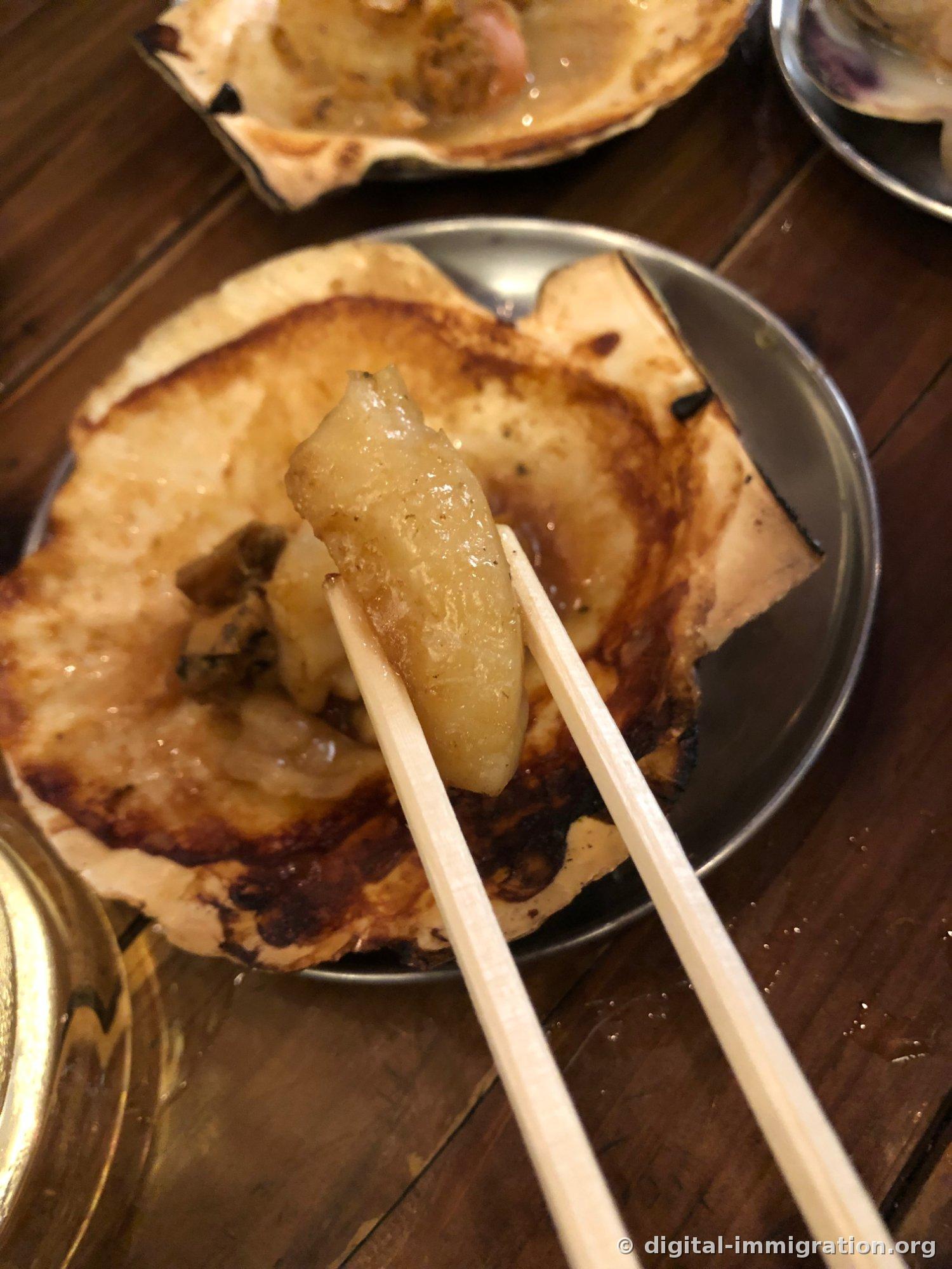 贝壳边缘已经焦黑，用筷子从扇贝贝壳上夹起一块贝柱的样子