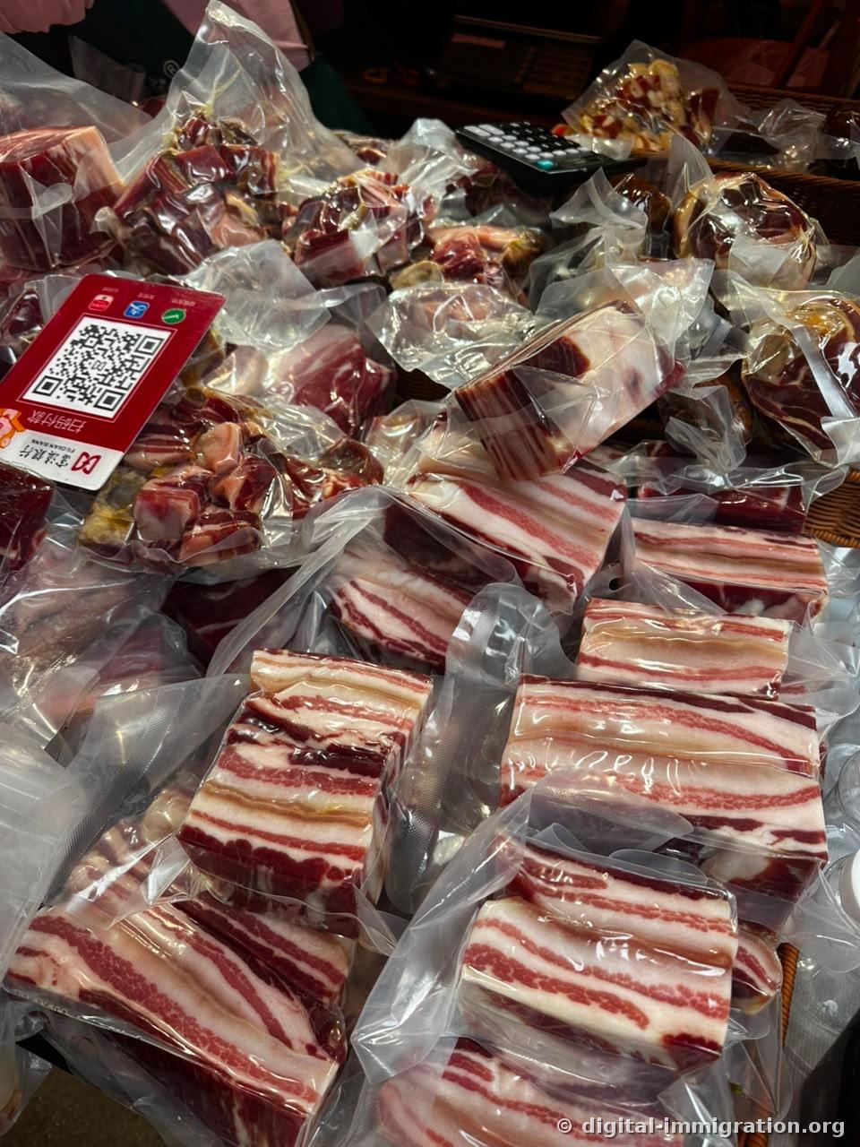 Mounds of vacuum-packed pork belly stacked on a meat counter with a red QR payment sign and black calculator
