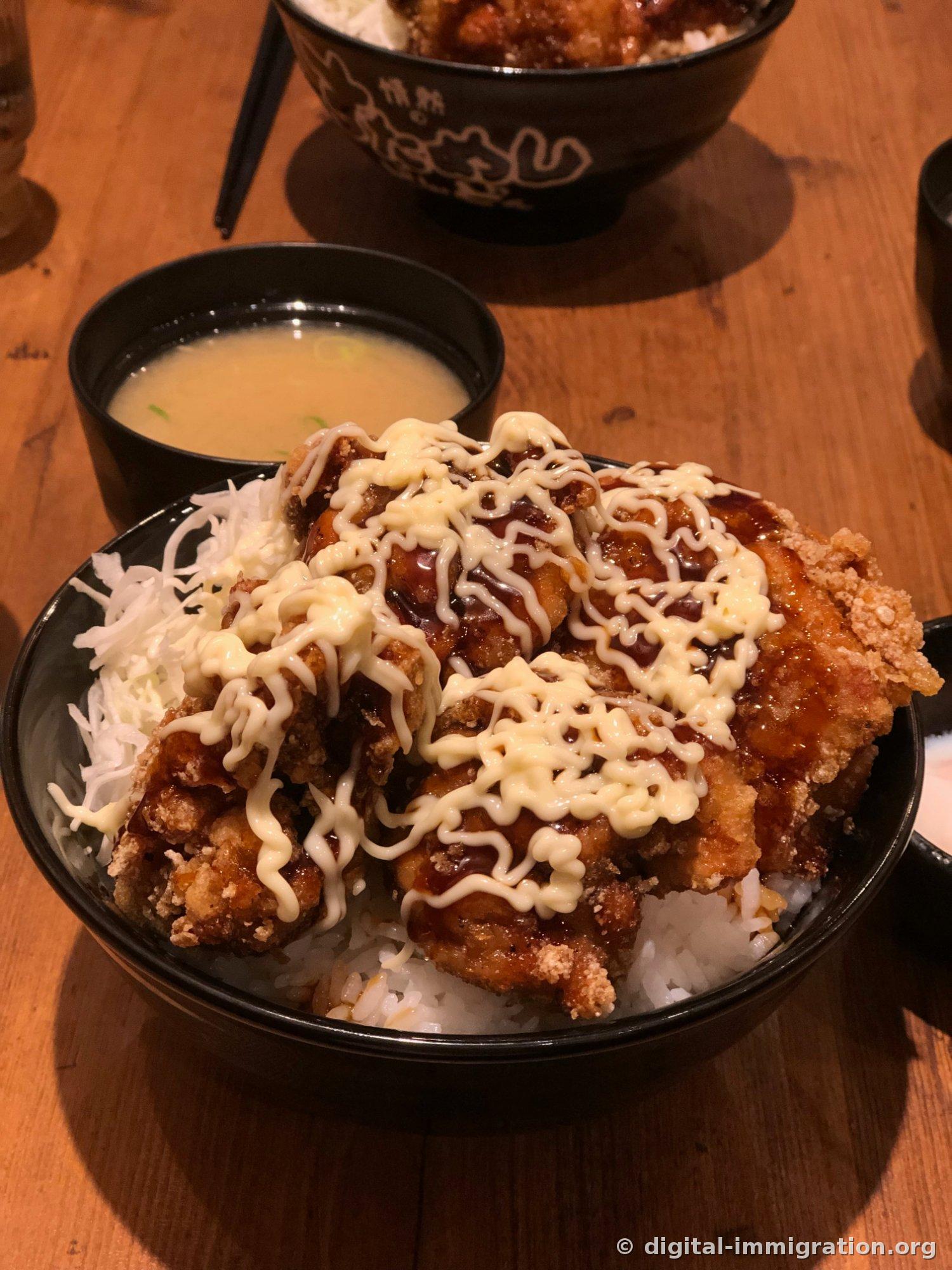 Chou finement tranché et riz avec poulet frit sur le dessus, garni de sauce marron et de mayonnaise en treillis, avec une soupe miso à côté et un autre bol noir de riz garni