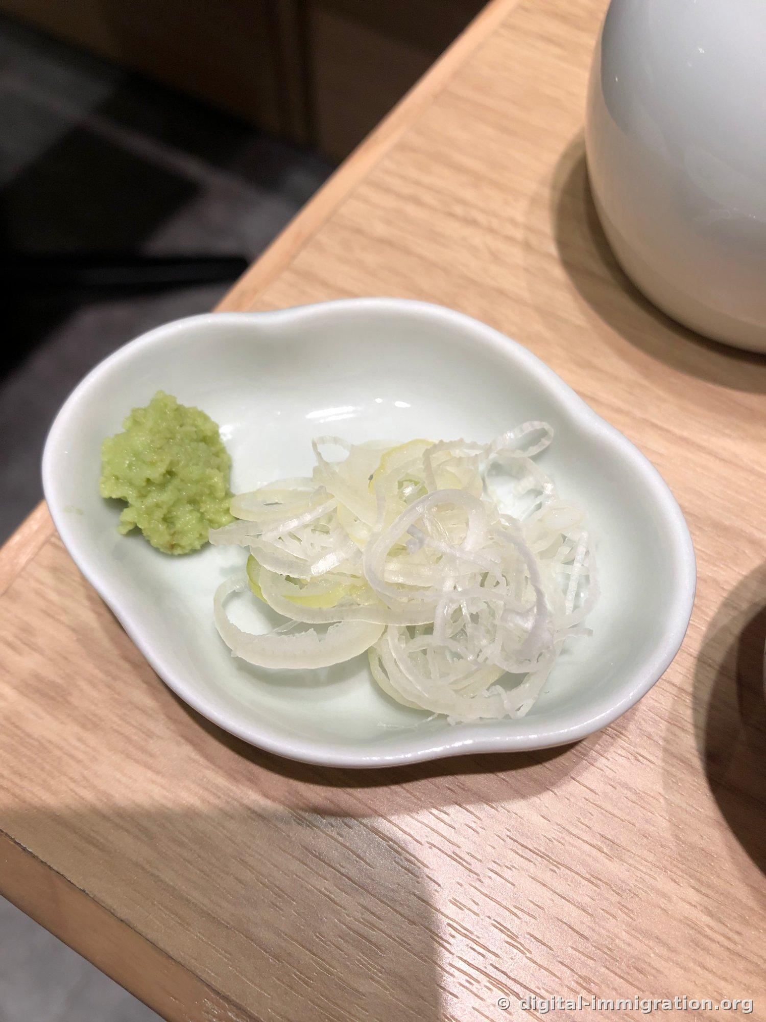 Grated wasabi and thinly sliced white scallions on a small white flower-shaped plate