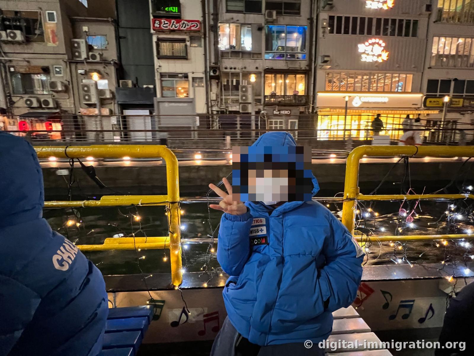 Les ampoules enroulées sur la rampe jaune du bateau et l'eau du fleuve, enfant en duvet bleu faisant le signe V devant l'enseigne de porc grillé de l'autre côté