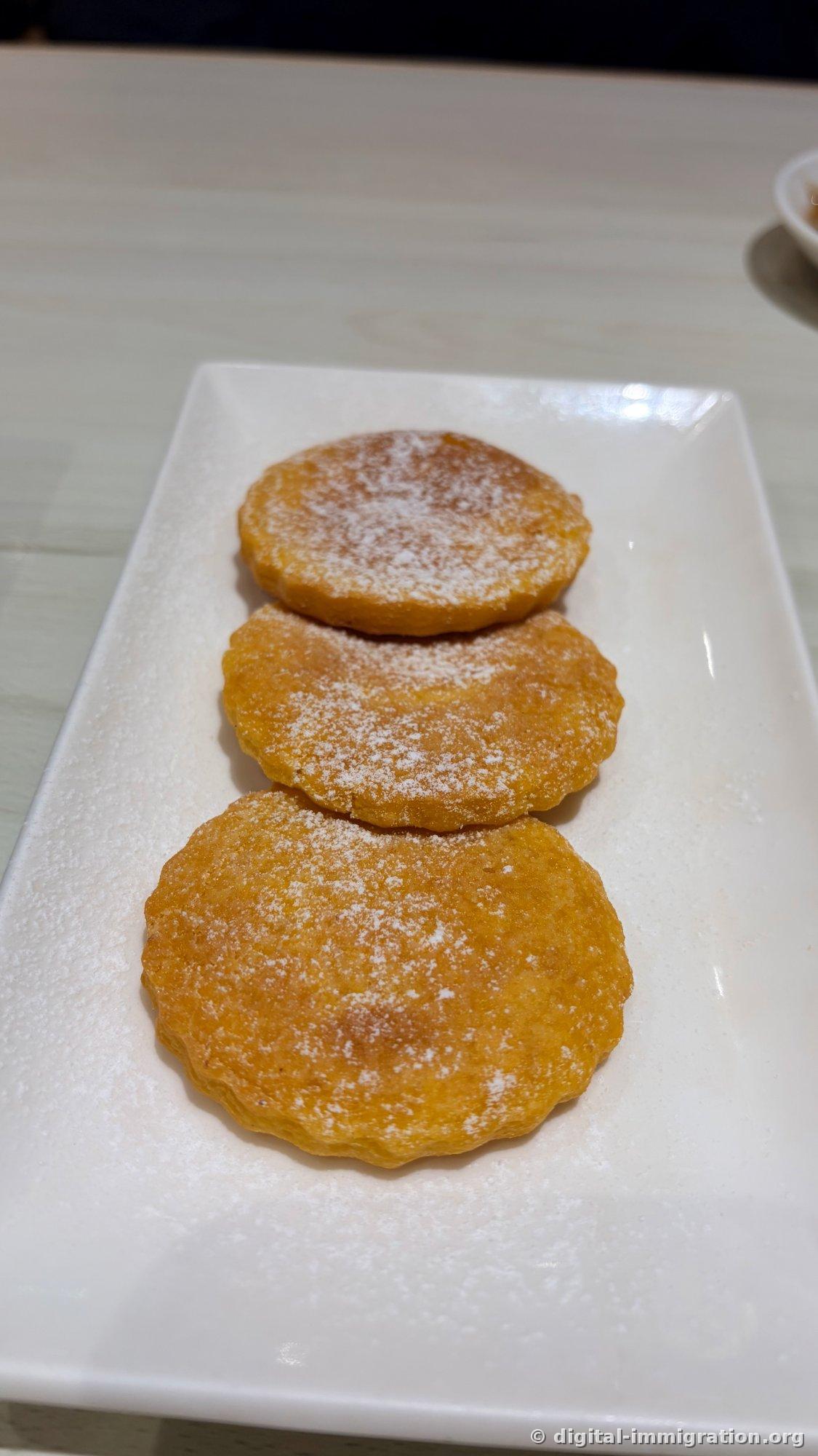 Three golden fried pastries dusted with sugar powder lined up on white rectangular plate