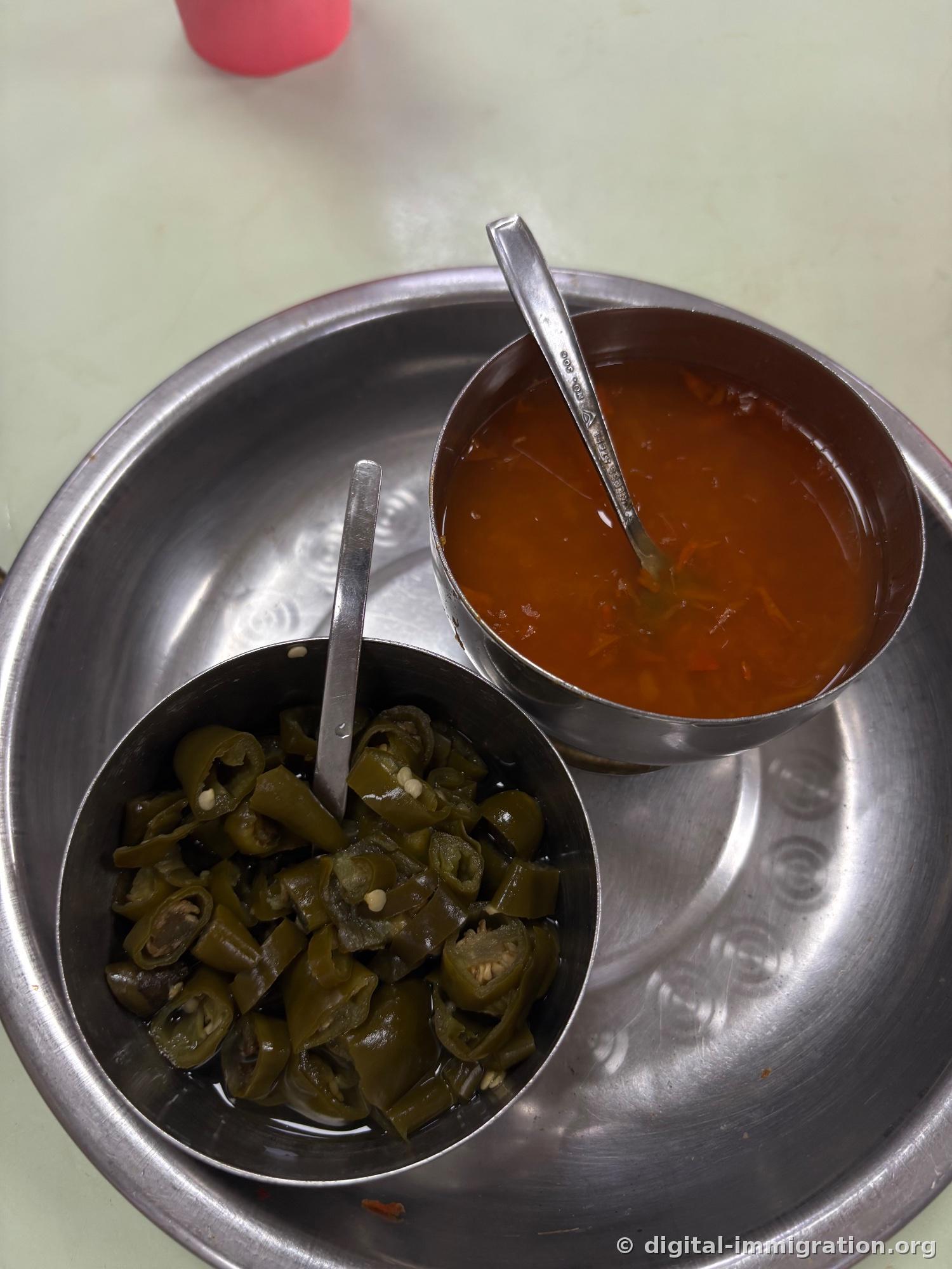 Deux pots de sauce sur plateau inoxydable, à gauche tranches de piments verts marinés au vinaigre, à droite sauce sambal orange avec cuillère
