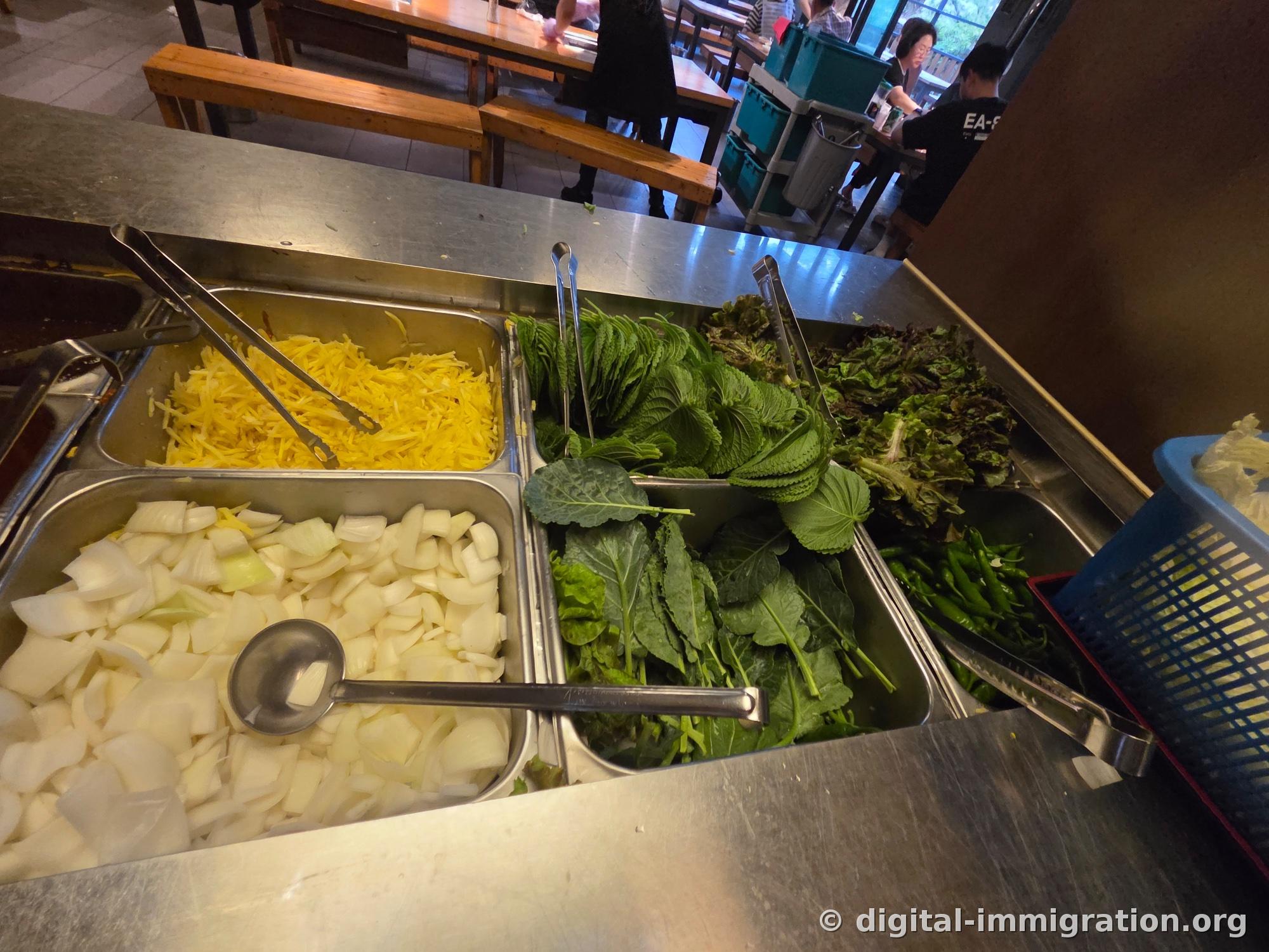 Les bacs en acier inoxydable du bar libre-service contenant les germes de gingembre jaunes, l'oignon trempé, les feuilles de périlla et la laitue, le chou frisé et les piments frais