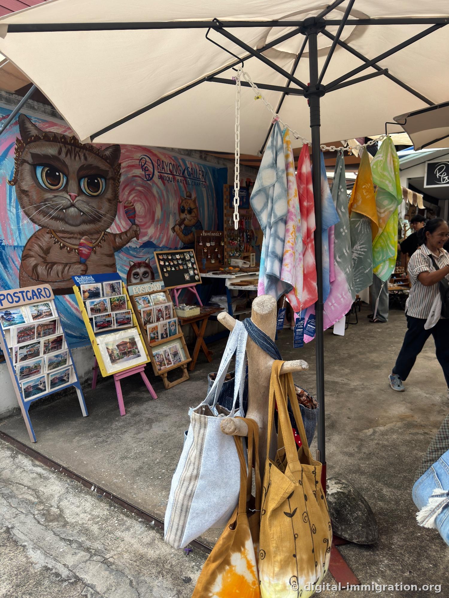 RAYONG GALLERY booth with large cat mural, postcard display and hanging hand-dyed scarves, eco bags