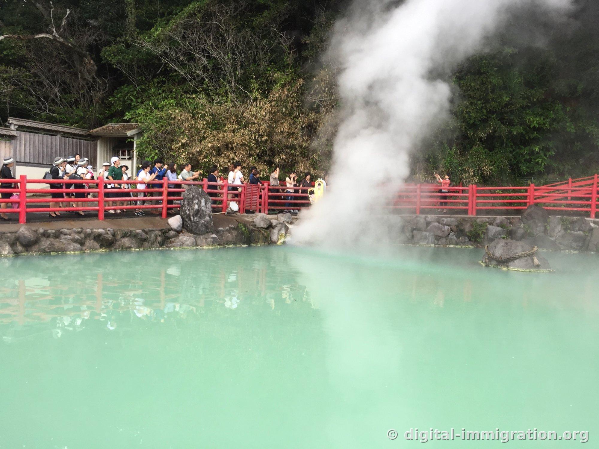 Des touristes en file le long de la rambarde rouge autour du bassin d'eau chaude vert laiteux, avec de la vapeur s'échappant