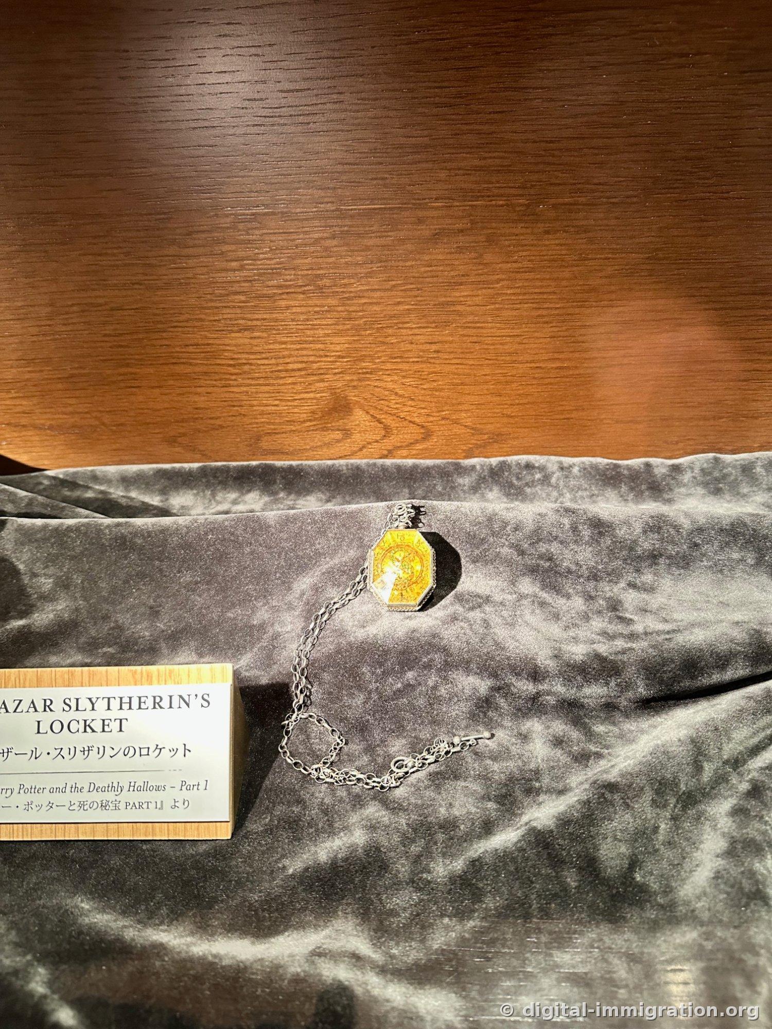 An octagonal gold locket with a long silver chain on gray velvet, with the nameplate SALAZAR SLYTHERIN'S LOCKET