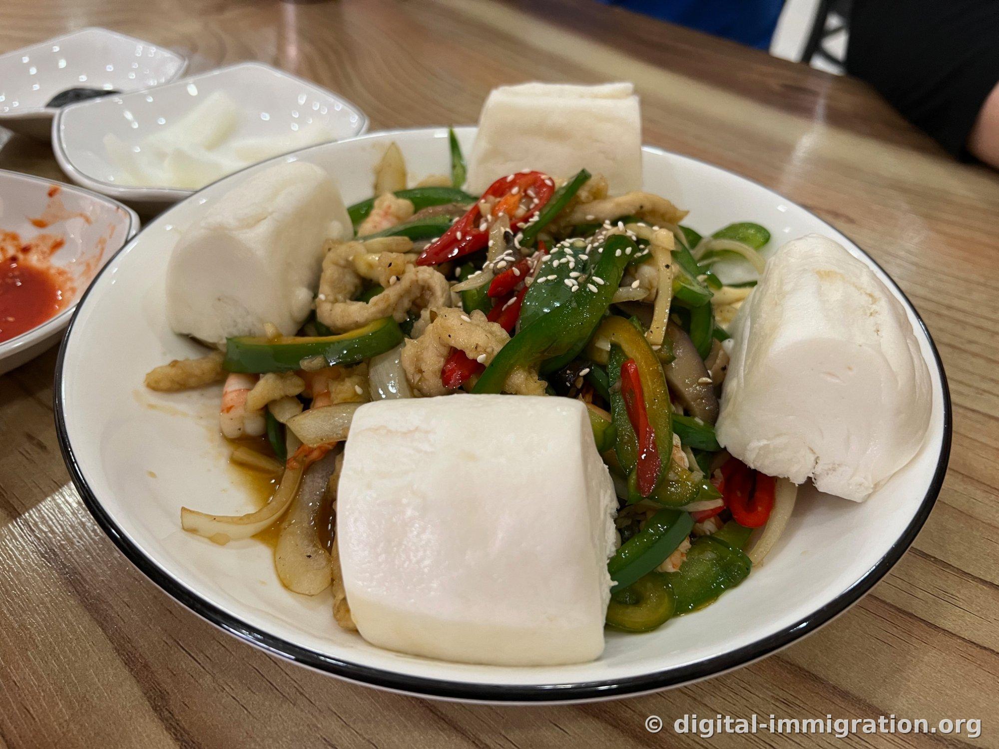 Stir-fried dish served surrounded by flower bread. Red chilies and green peppers are vibrant throughout.