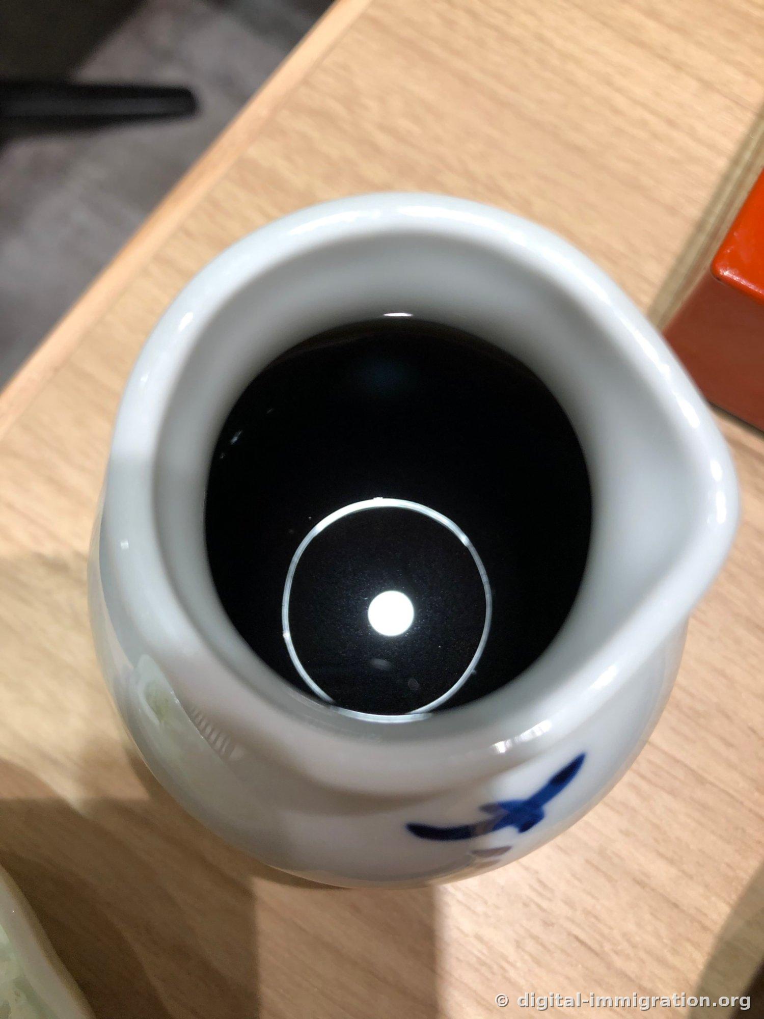 Looking down into a white porcelain pitcher filled with nearly black tsuyu dipping sauce