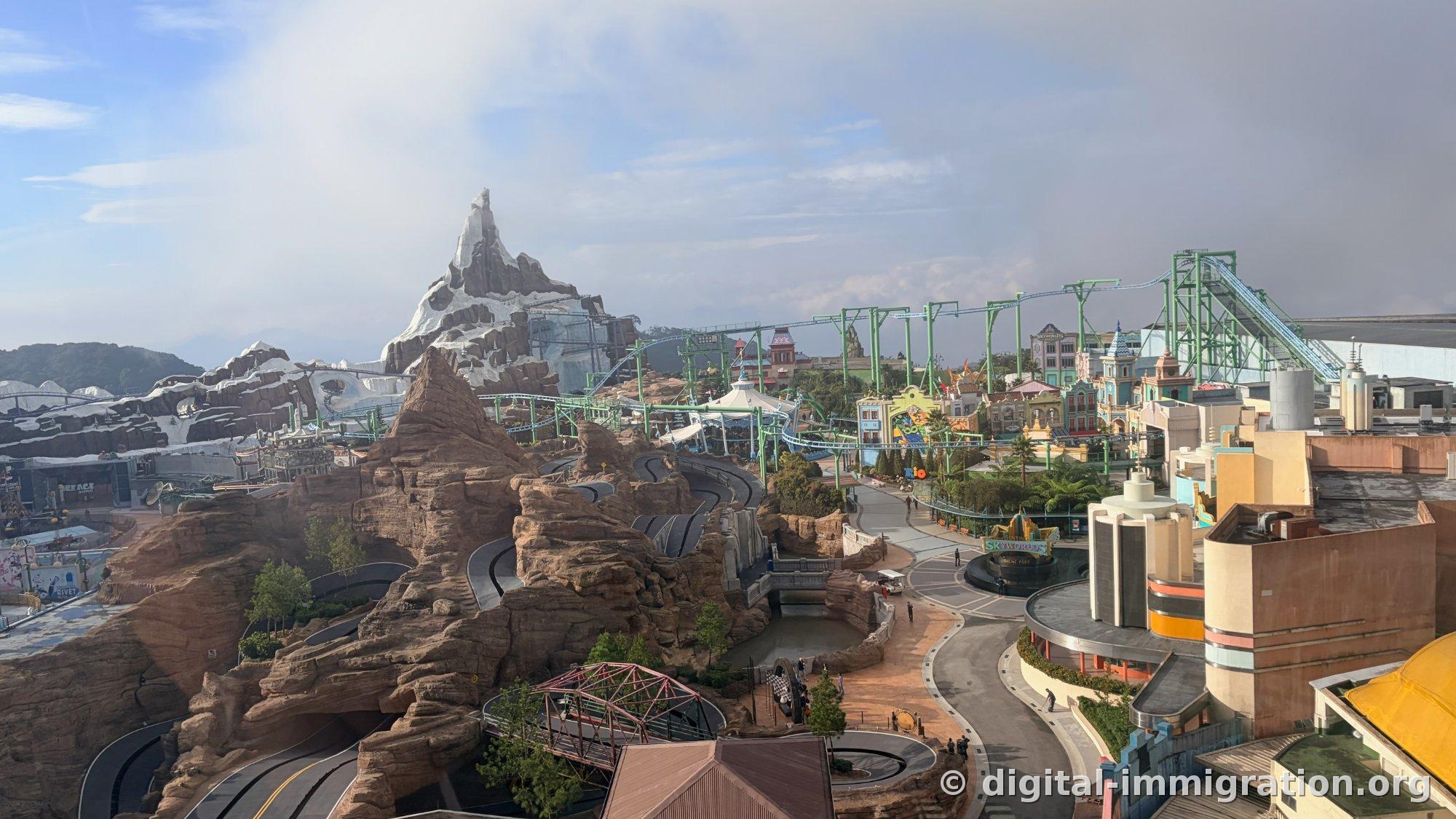 Full panorama of Genting SkyWorlds with artificial snow mountain and canyon track, green coaster rail, real mountain ridge and clouds behind