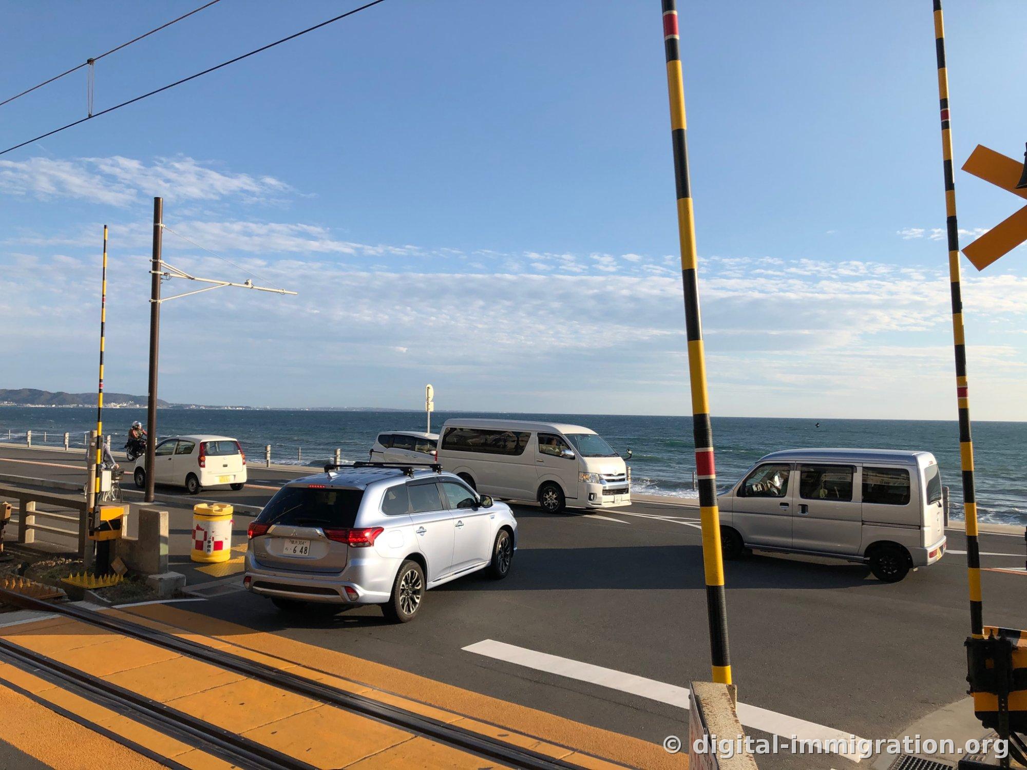 Au-delà de la barrière à rayures jaunes et noires, les voitures traversant la route nationale 134 avec la mer bleue de Sagami en arrière-plan