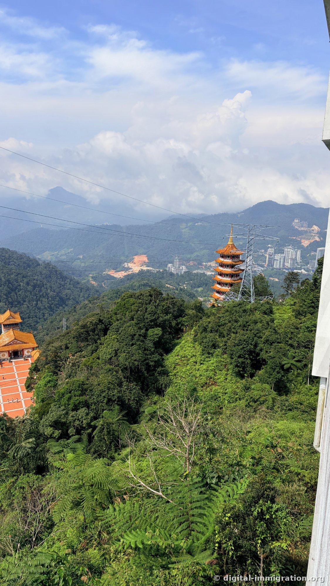 Vue d'une vallée de forêt tropicale depuis une hauteur, la pagode de 9 étages debout au milieu, avec des pylônes électriques à droite et des immeubles de grande hauteur de Genting en développement au-delà de la crête