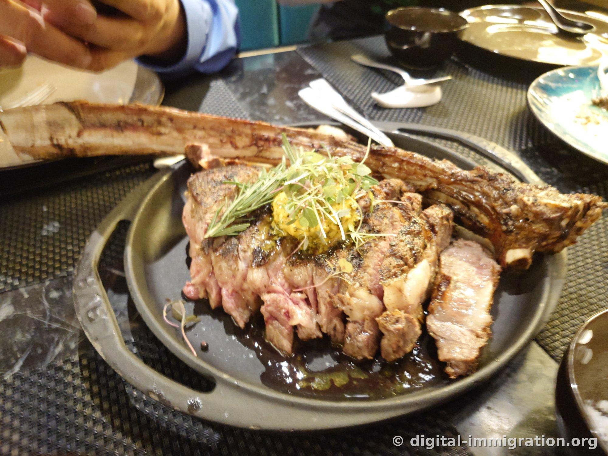 Tomahawk steak with long bone sliced and fanned out, topped with herb butter and rosemary on a metal plate
