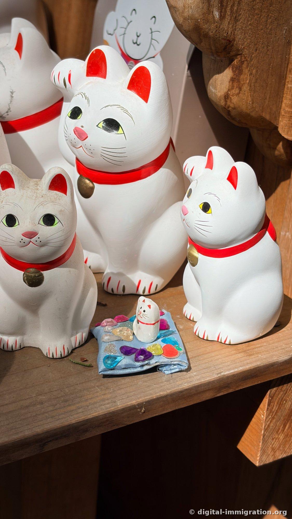 A small handmade blue cloth cushion with colorful gem stickers in front of three cat figurines, with a tiny cat sitting on top