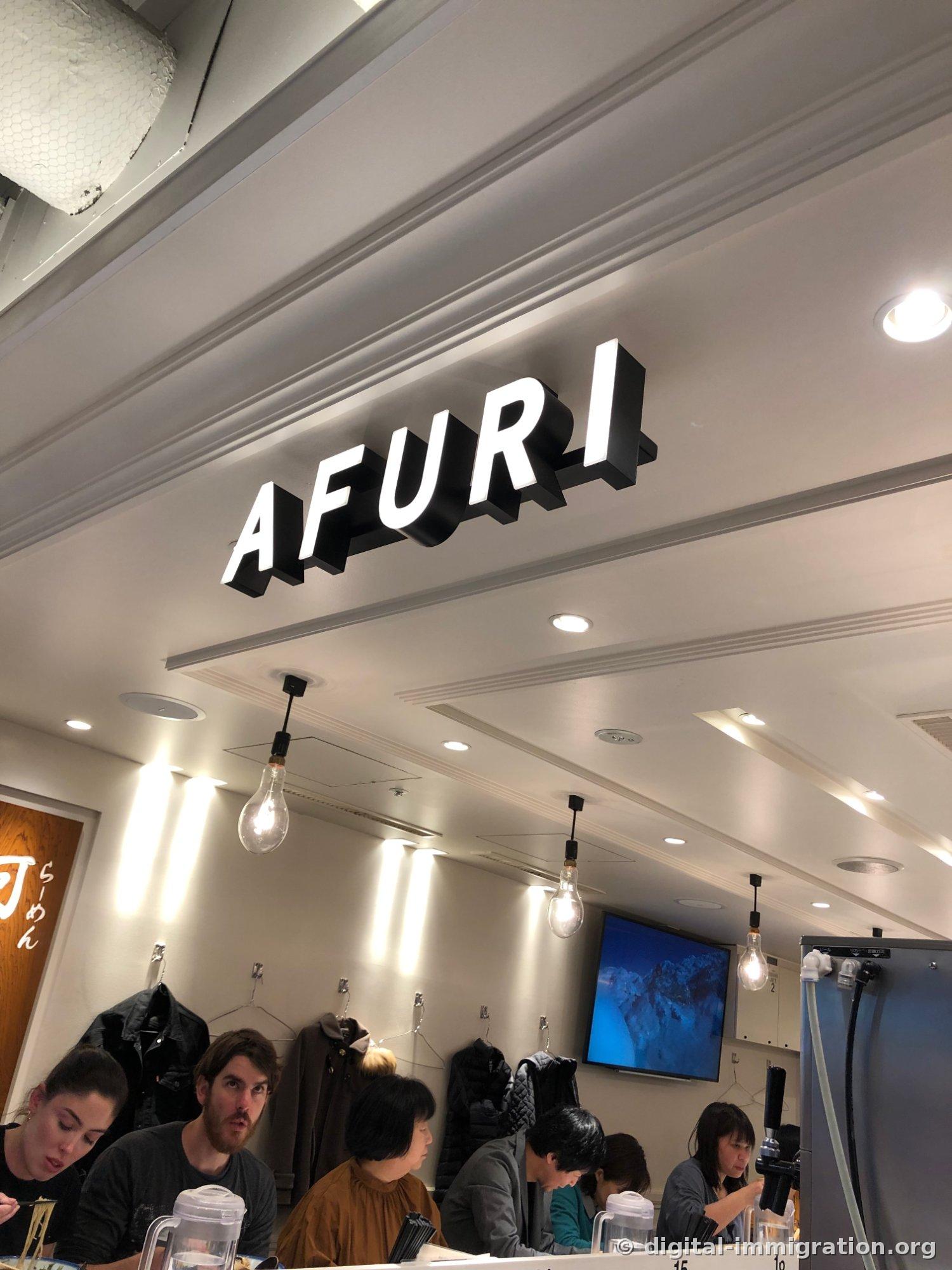 3D AFURI letters on a black background hanging from the ceiling with light bulbs below, and customers eating ramen at the counter