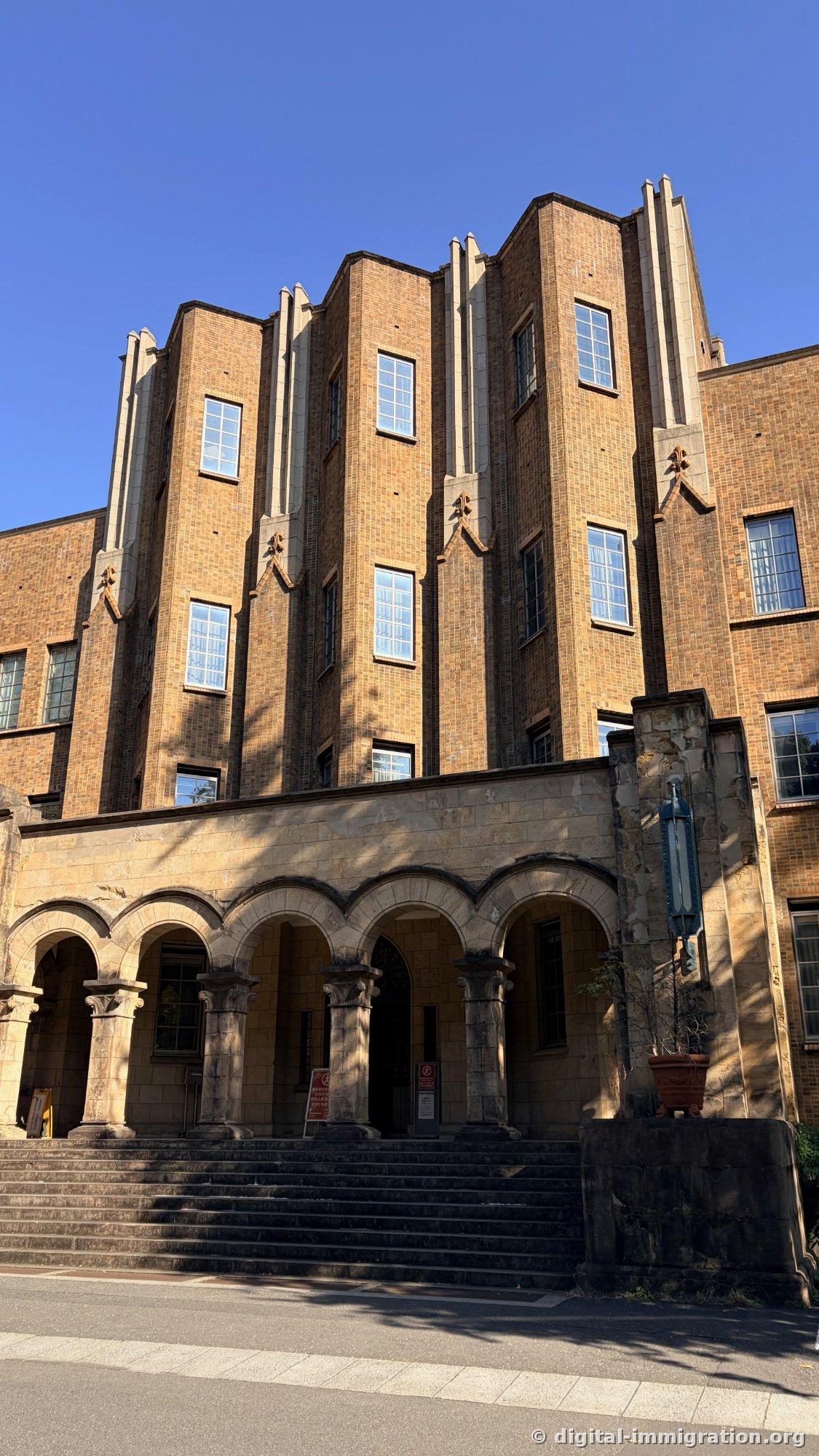 Brick building facade with arcade colonnade atop the stairs, capitals carved with ornament and blue sky reflected in windows
