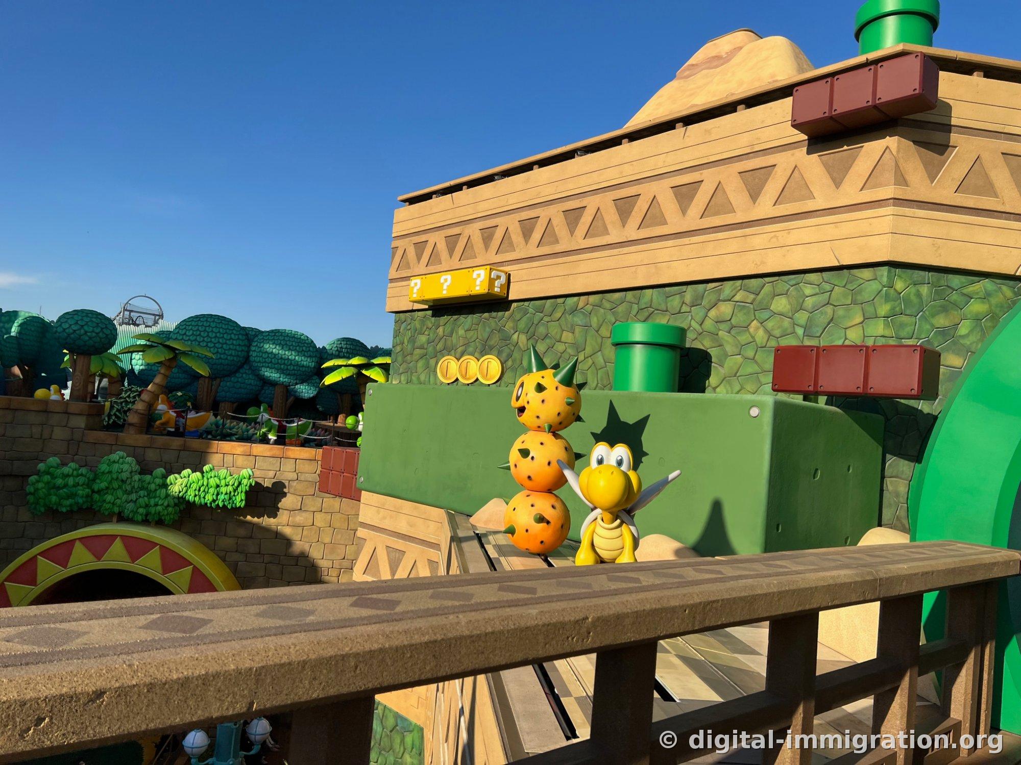 Three-tiered orange Spiny shell sculptures beside the ride track and a yellow Koopa Troopa character with raised hand, with three question mark blocks above