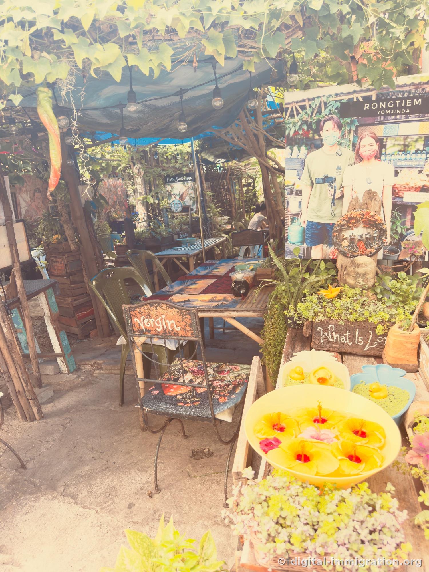 Outdoor seating under vine shade, hibiscus flowers floating in yellow basin and rubber duck, RONGTIEM YOMJINDA sign