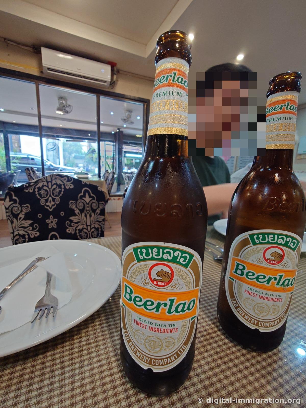 Two brown bottles of Beerlao Premium on the table, with the wall-mounted air conditioner and glass window visible in the background
