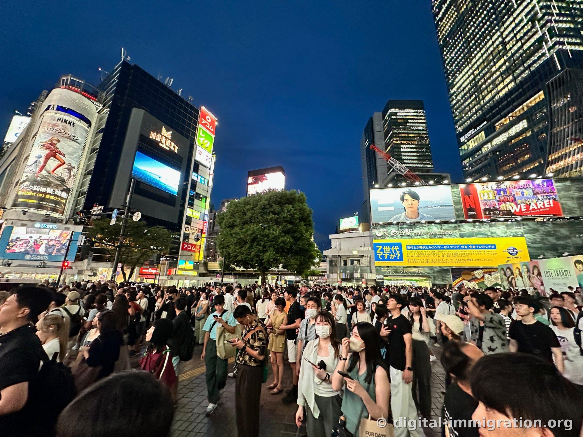 夜の渋谷駅前広場を埋め尽くす人混み、黄色いZ世代の広告バナーとネットフリックスの屋外広告、クレーンが一緒に見える