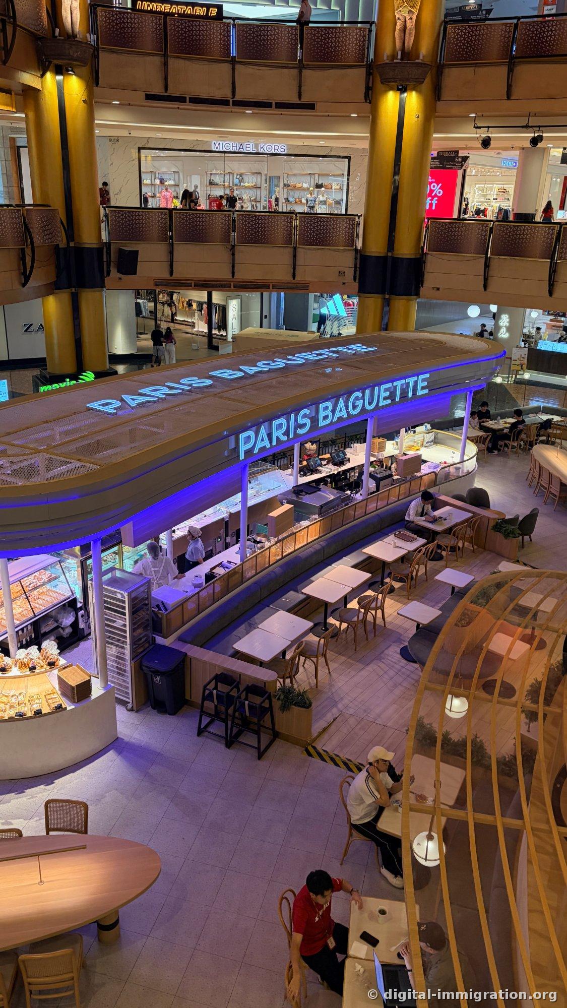 位于商场中央的蓝色霓虹招牌 Paris Baguette 店铺和上层的 Michael Kors、ZARA 店铺