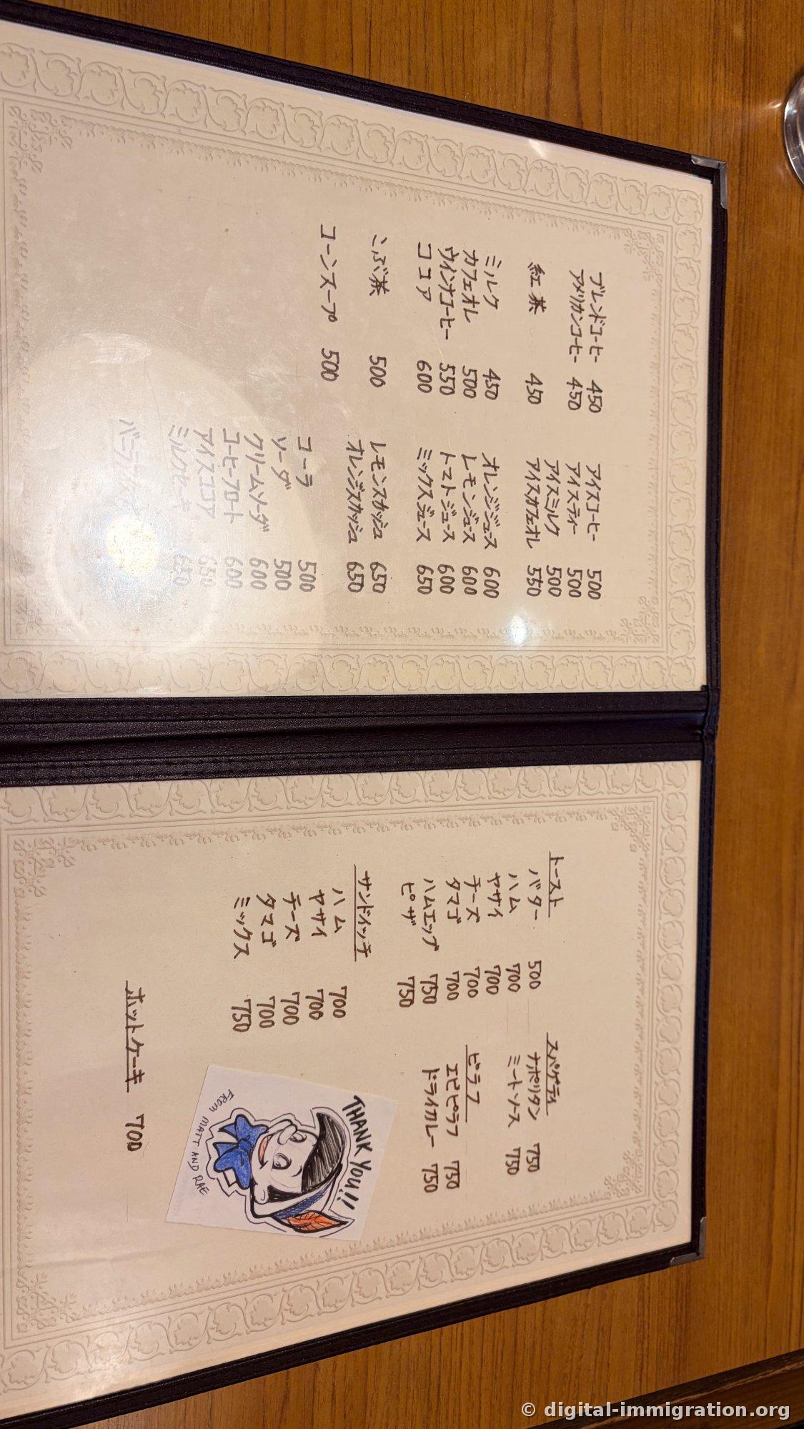 A handwritten vertical-text menu spread on a wooden table with drink and toast prices, and a hand-drawn THANK YOU sticker in the bottom right