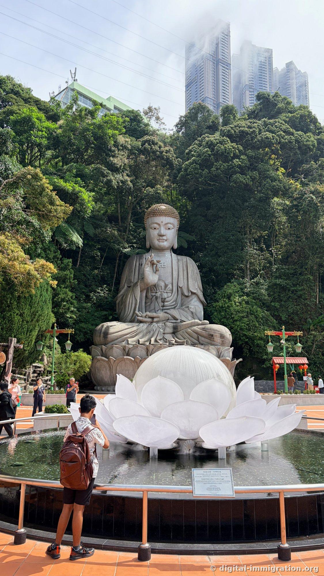Un grand bassin rond avec une sculpture de lotus blanc semi-transparent au centre, un homme avec un sac à dos prenant une photo