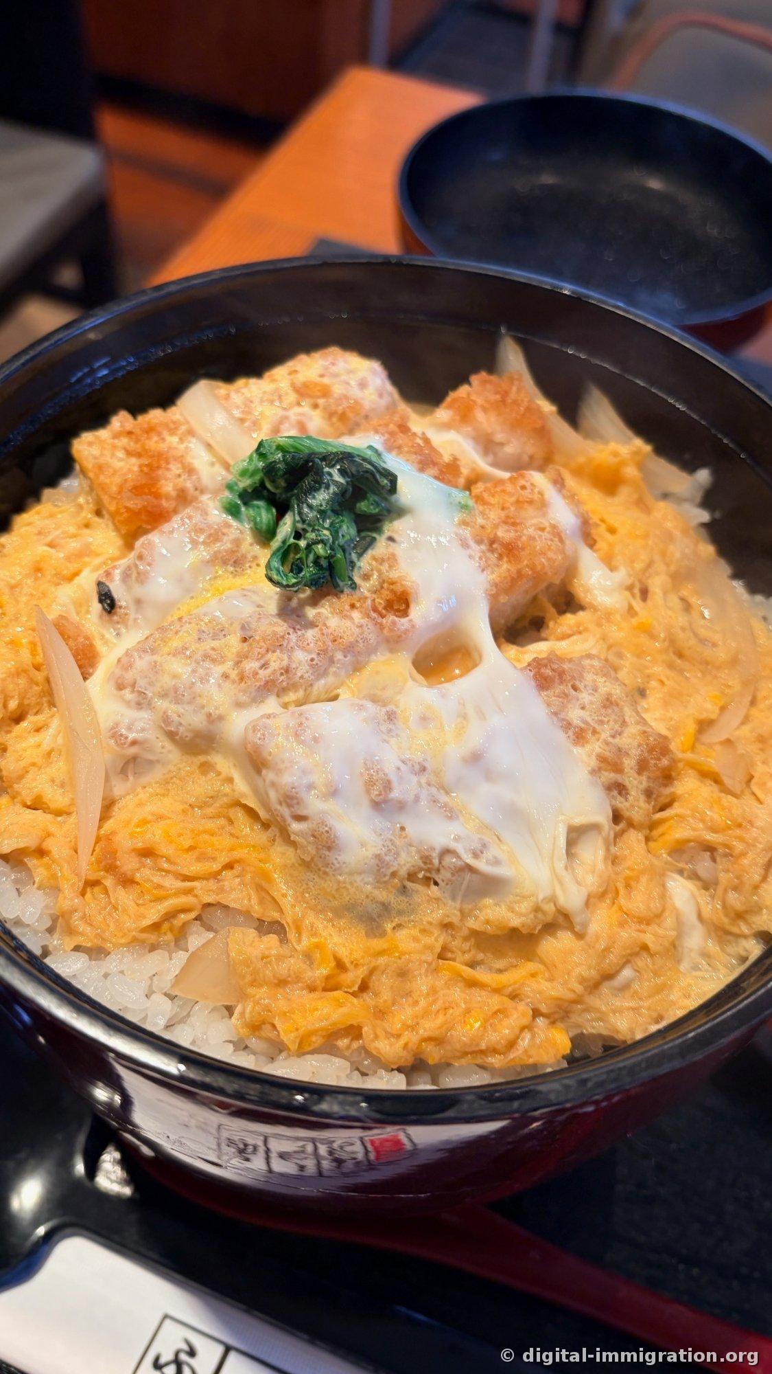 Katsudon dans un bol noir. Un tonkatsu avec pâte frite vivante recouvert d'un œuf à moitié cuit et d'oignons finement tranchés, avec des épinards blanchis au centre