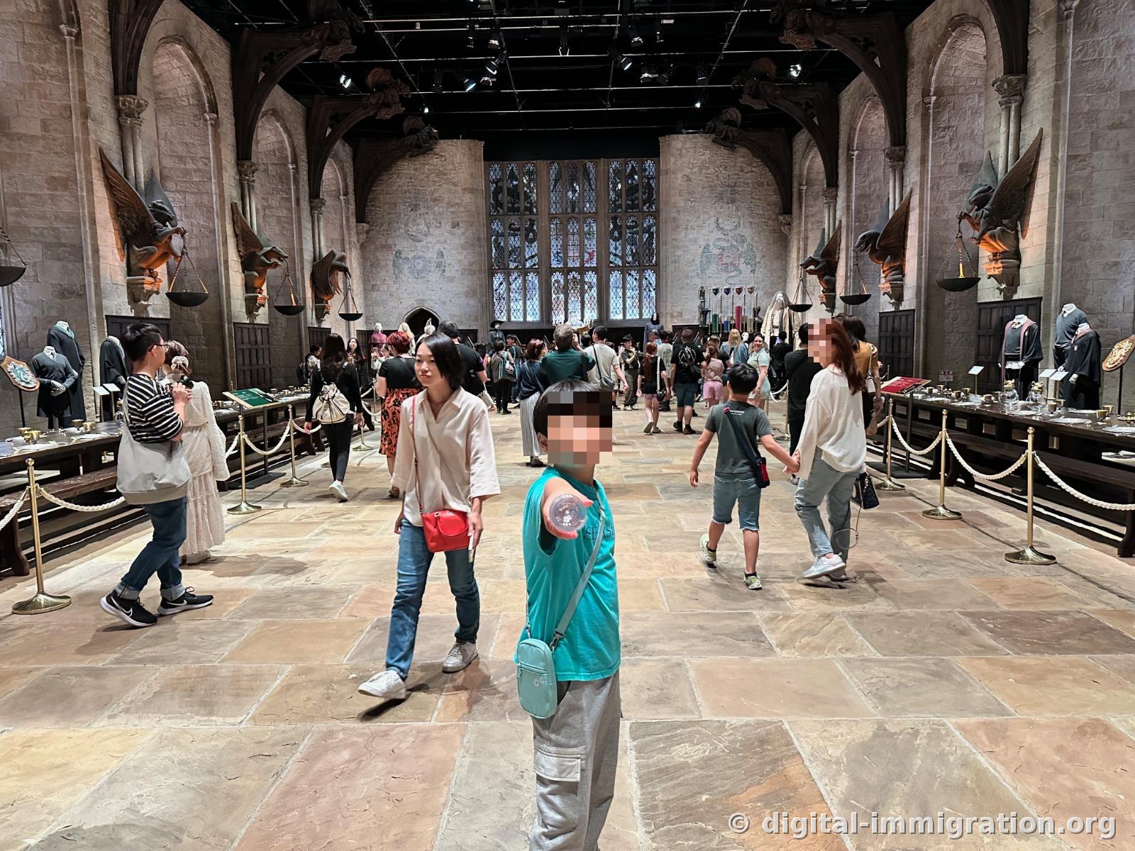Visitors walking inside the Hogwarts Great Hall set, with eagle sculptures and torches on the walls and tableware on long tables