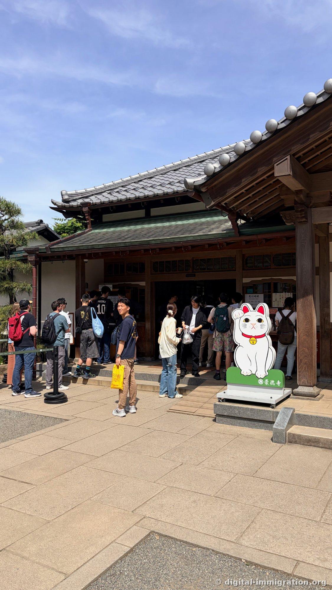 People standing in line before the offering hall of Gotokuji with a large signboard of white beckoning cats