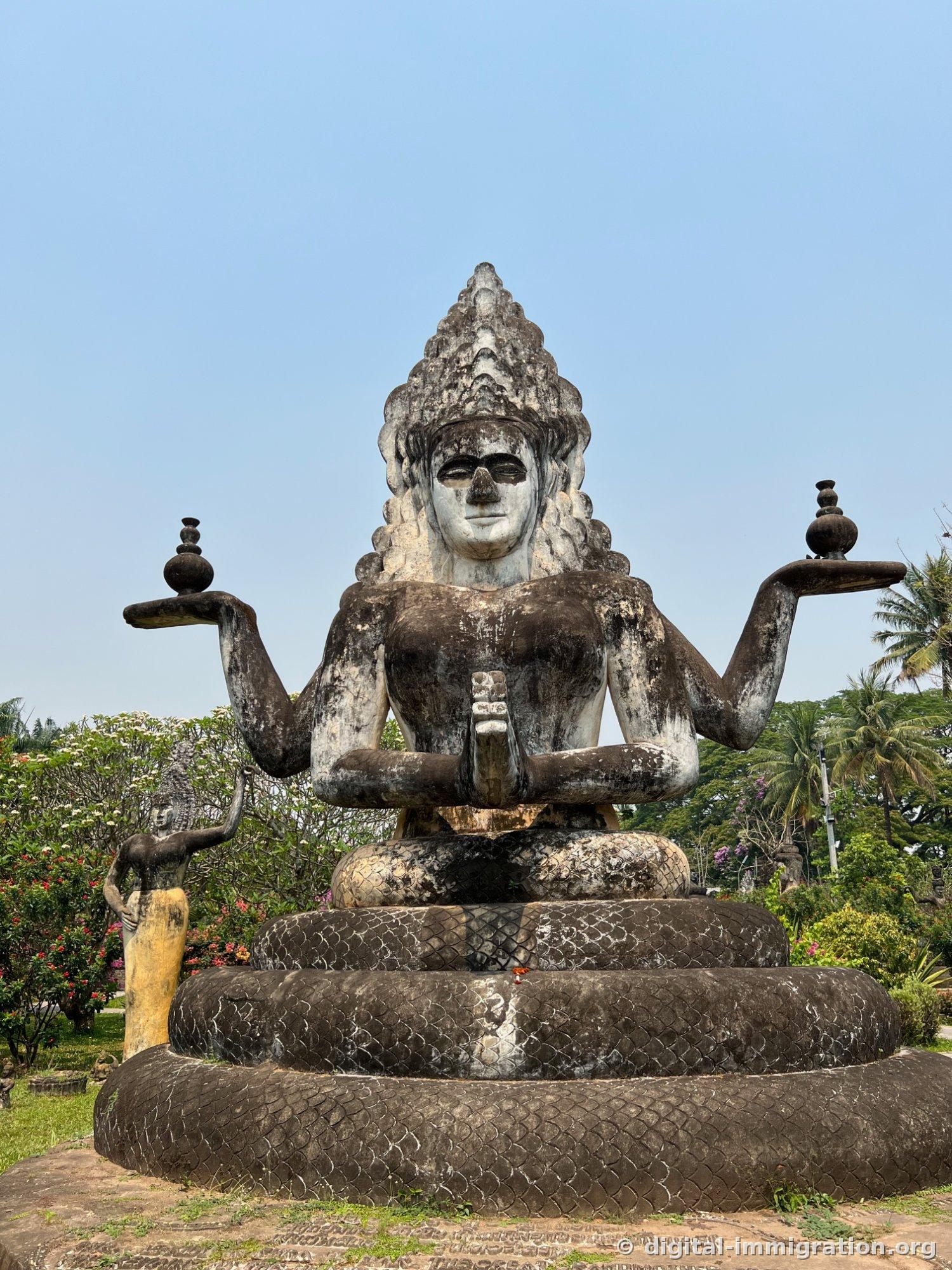 Une statue assise multibras sur un corps de naga enroulé en trois niveaux, avec le visage blanc et le corps noir profond