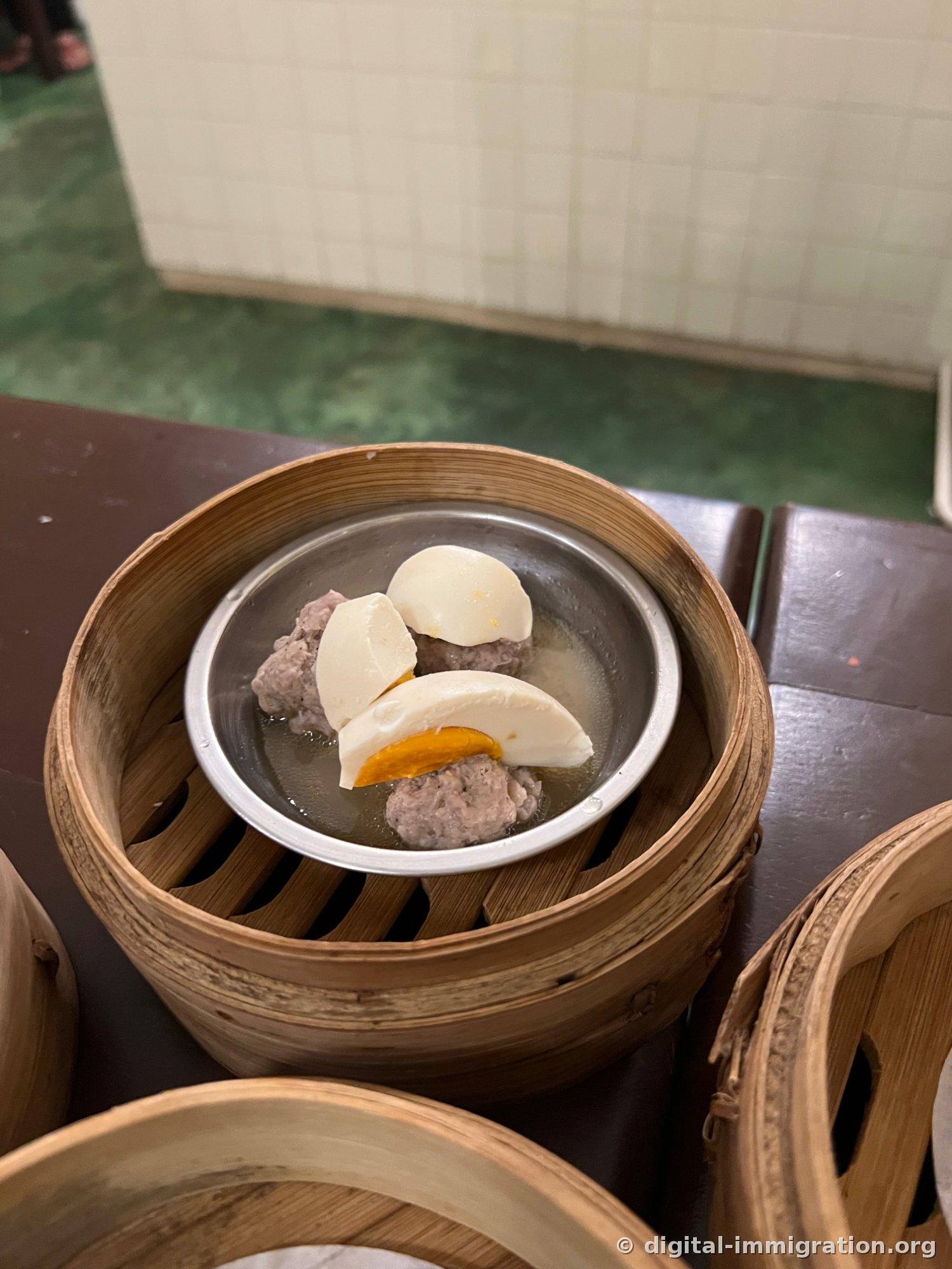 竹のせいろ内の銀色の皿に豚肉団子と半分に切った茹で卵の切れ端がスープとともに入っている