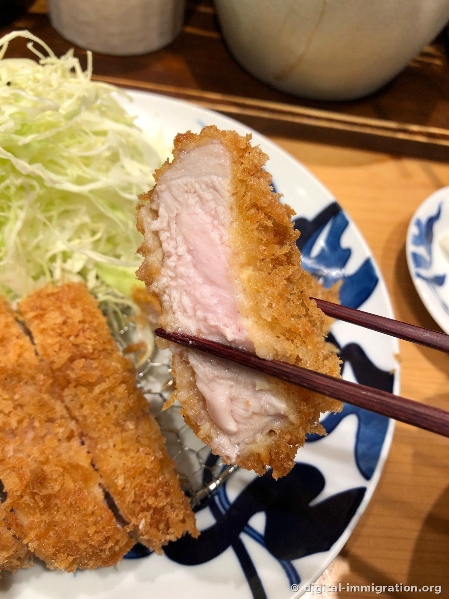 用筷子夹着的里脊肉炸猪排单面。炸衣下面的肉呈淡粉红色