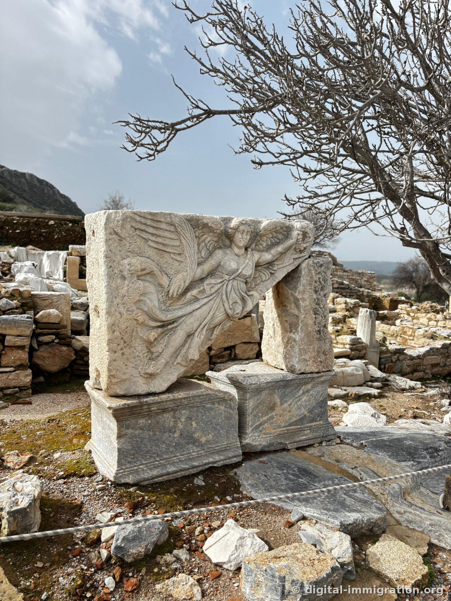 A marble relief of the goddess Nike with wings spread and holding a wreath is placed on a stone base