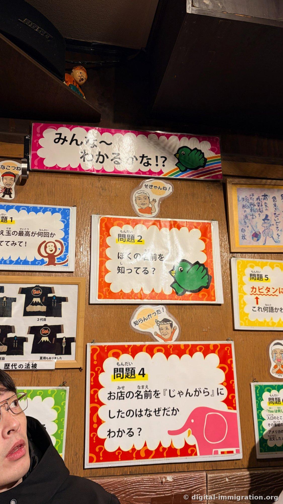 Quiz posters on the shop wall, pink banner reading Everyone-Can-You-Figure-This-Out with problem cards 2, 4, and 5, and framed photos of hapi jackets from different eras hung together