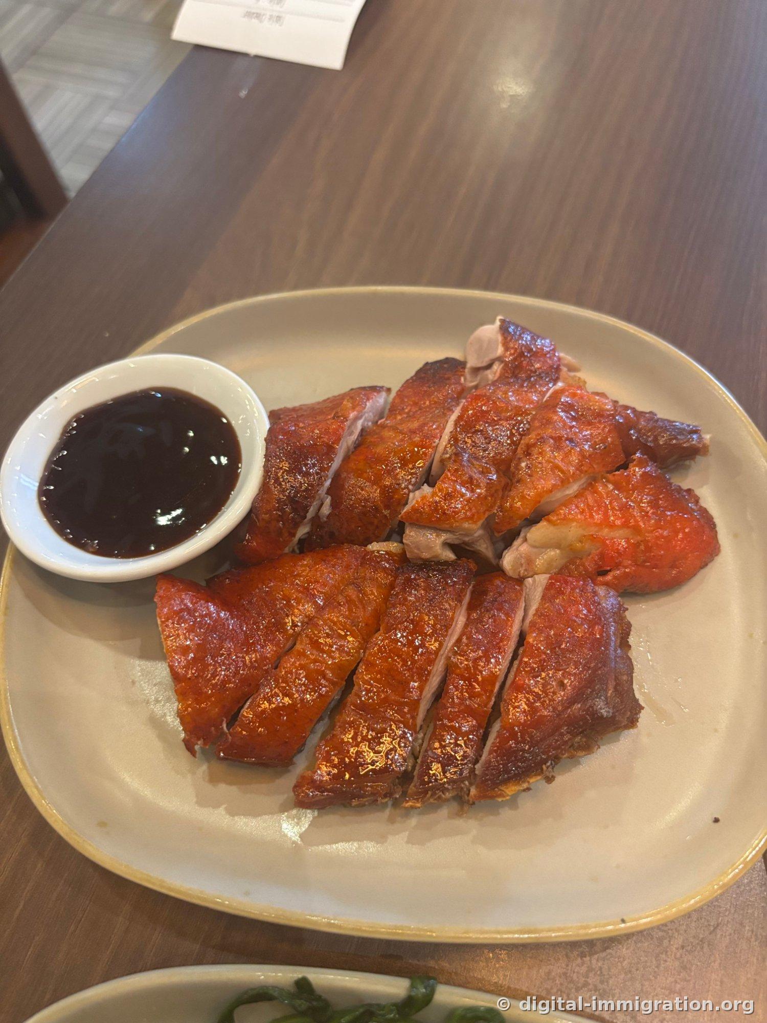 Slices of glossy red smoked duck fanned out on a plate, with a bowl of dark sauce on the left