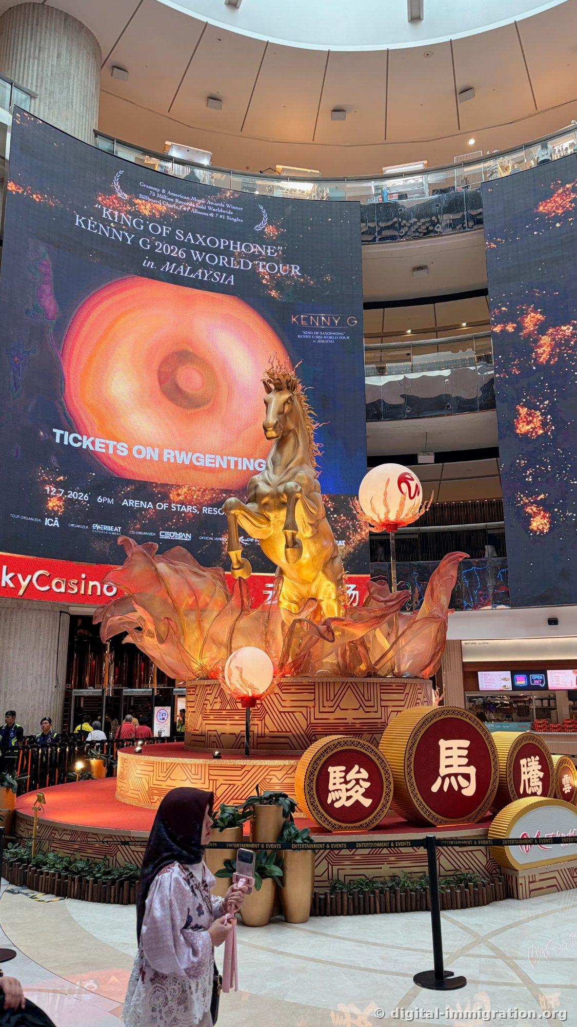 Large LED screen displaying KENNY G 2026 WORLD TOUR in MALAYSIA performance information with golden horse sculpture and red decoration circle in front