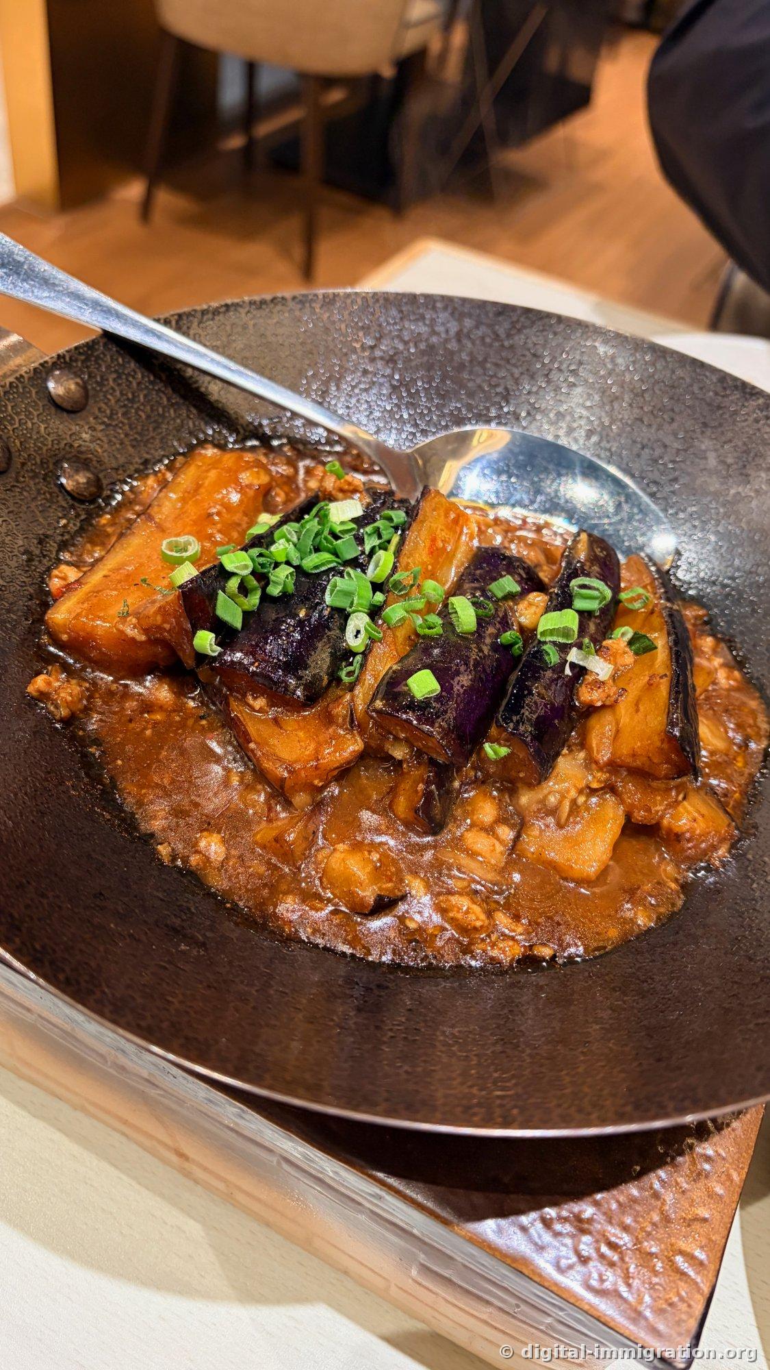 Fish-fragrant eggplant stir-fry in black wok with minced meat sauce and braised eggplant topped with scallions
