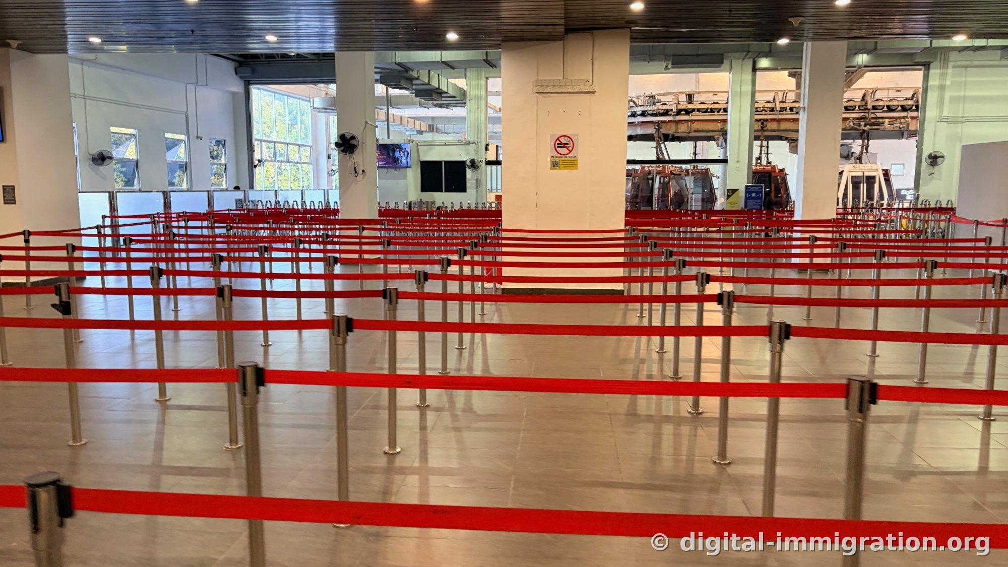 Empty cable car queue with multiple layers of red queue barriers and red gondola cabins waiting inside