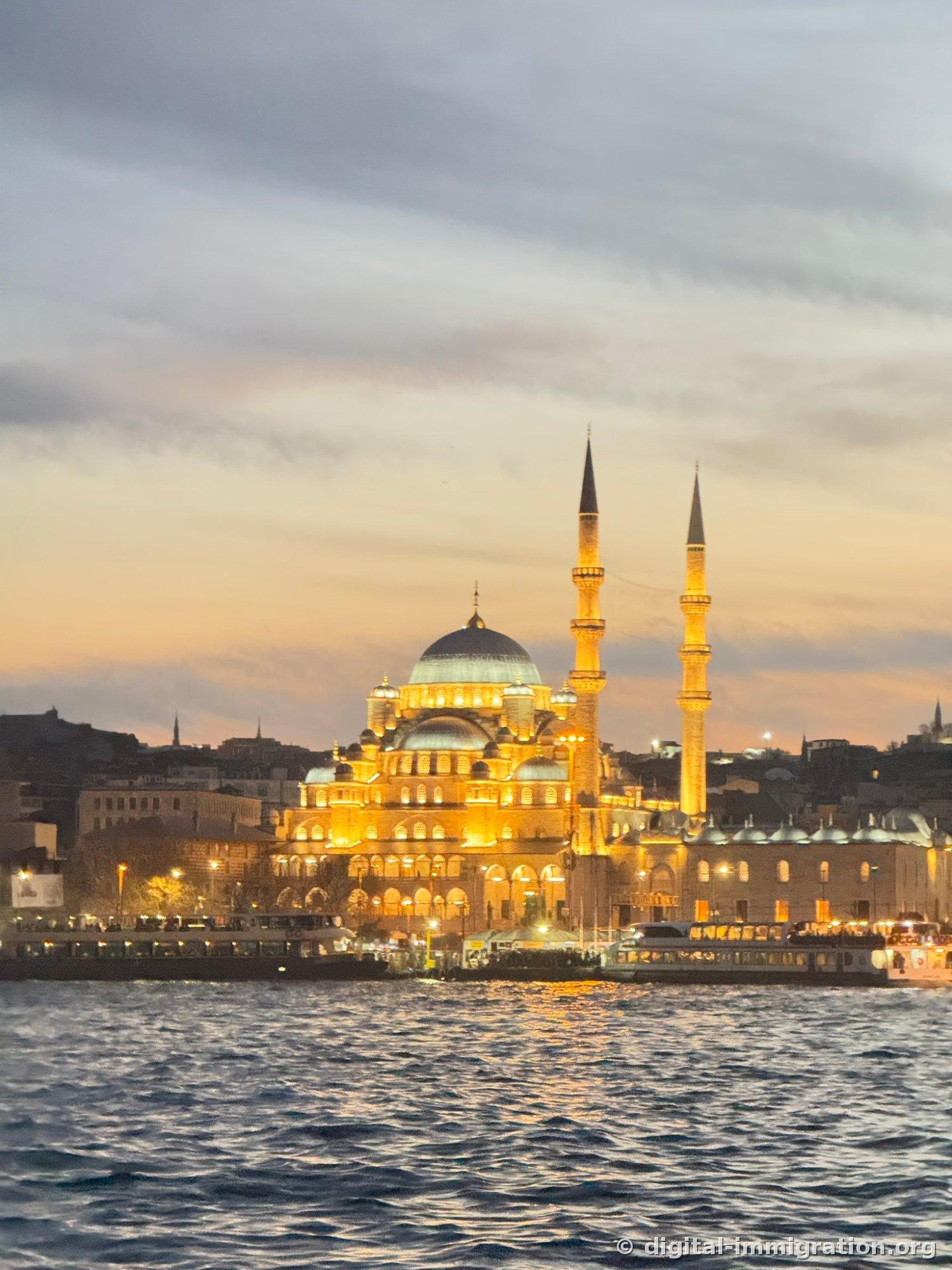 Yeni Cami with golden lights after sunset and two minarets, passenger ships moored below it and dark sea