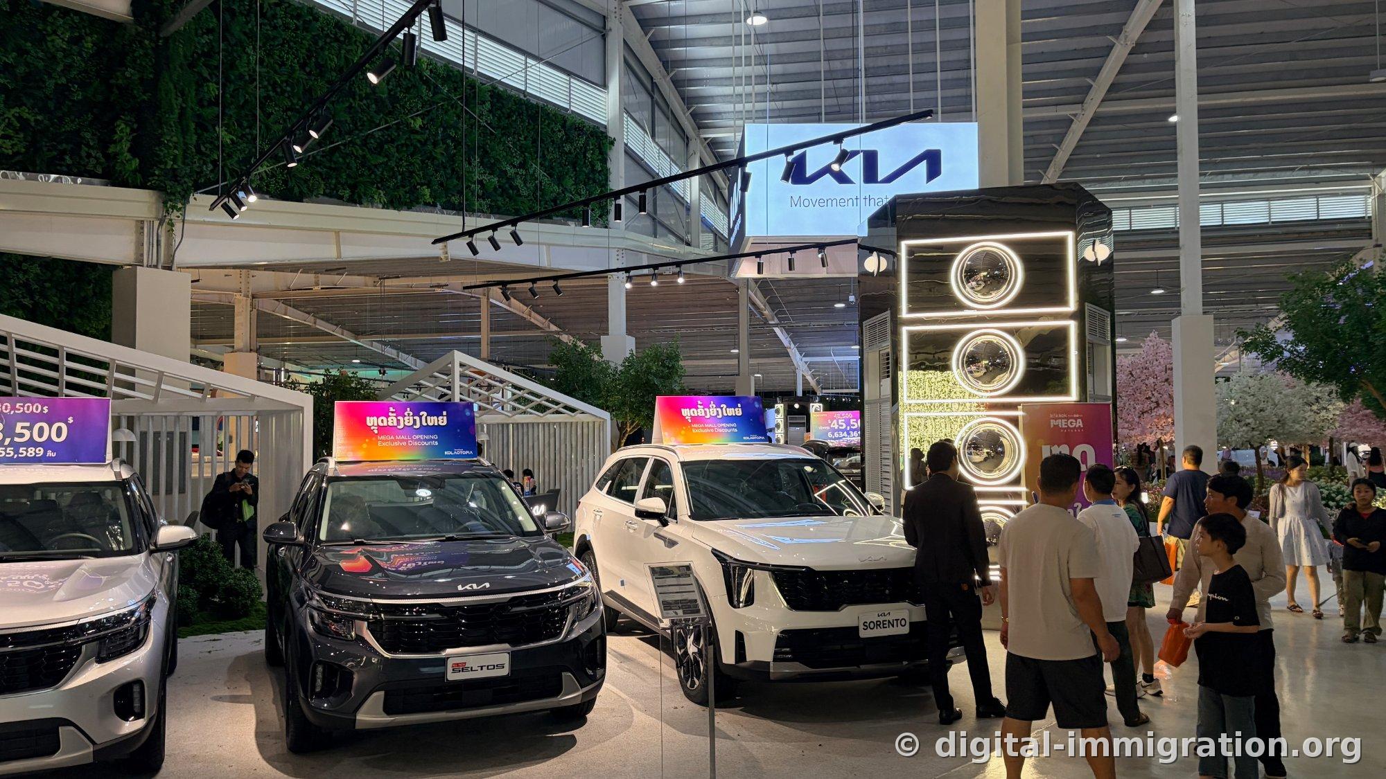 Kia display booth with black Seltos and white Sorento side by side, opening promotion discount sign on top of car