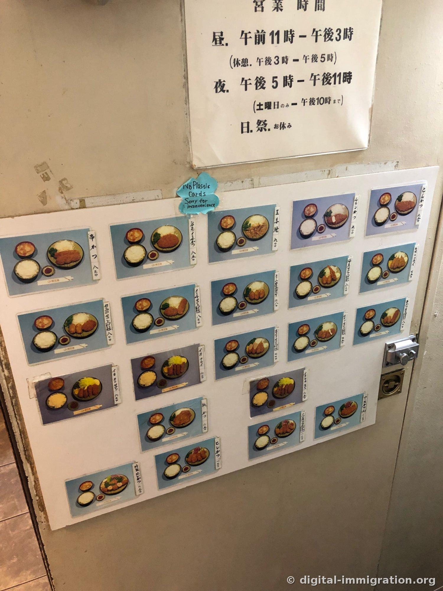 Business hours posted above the shop door, with laminated menu photos attached to the door itself. A blue flower-shaped handwritten note reading 'No Plastic Cards' is affixed above the menu photos